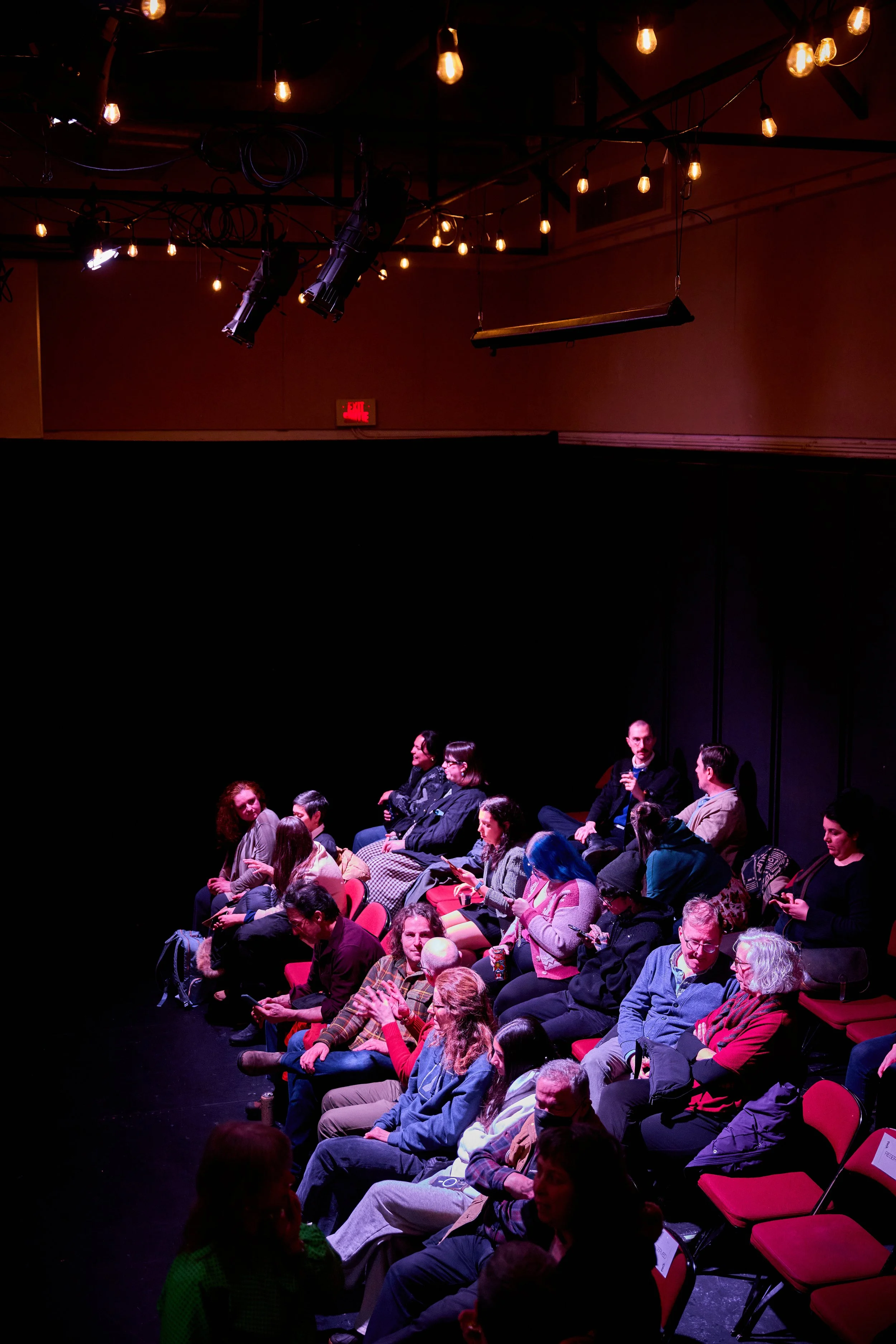 Auditorium avec des personnes assises, éclairage tamisé avec lumière chaude et décor de filaments lumineux au plafond.
