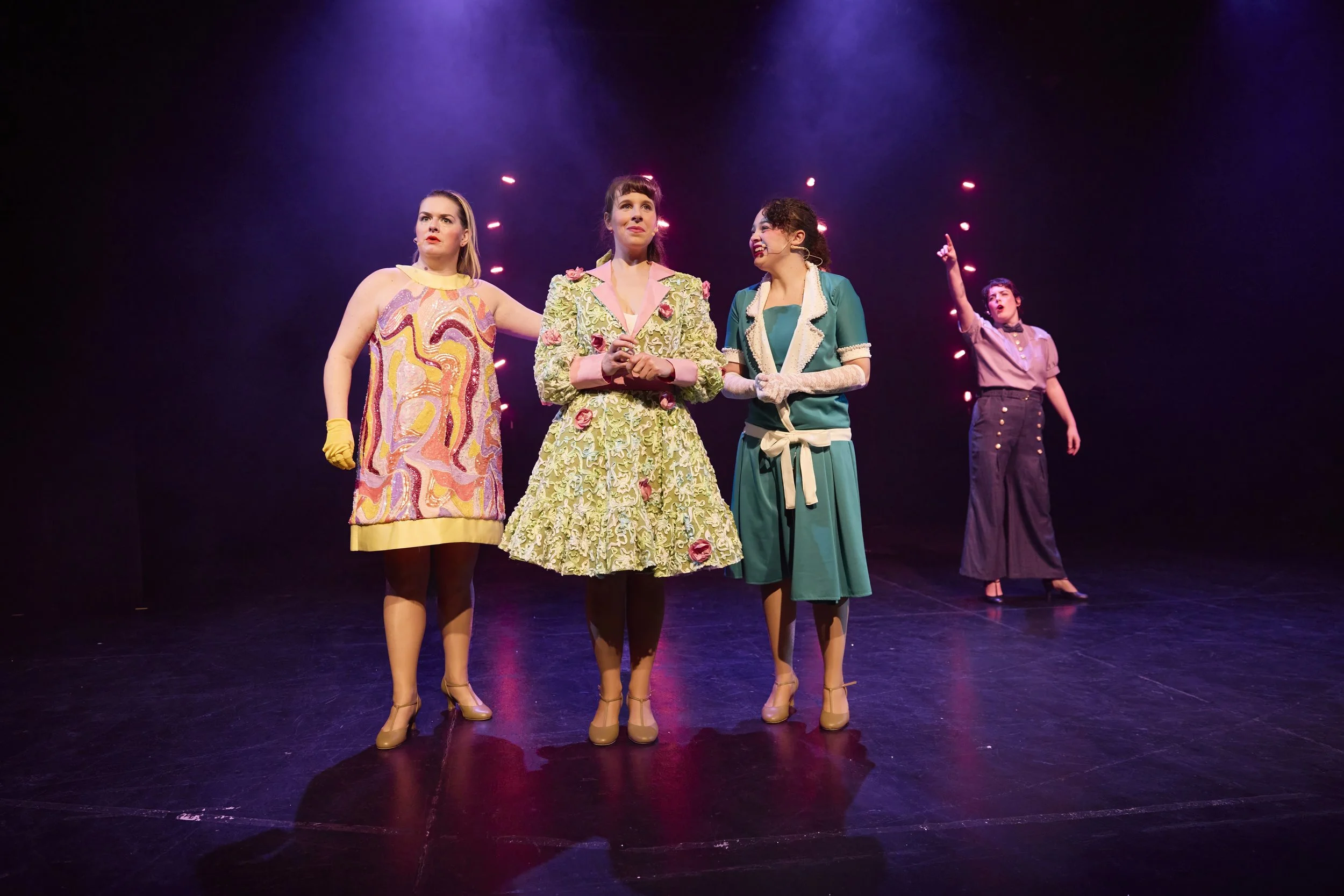 Créations In Vivo. Quatre femmes en costume sur scène avec éclairage violet, faisant une performance théâtrale.