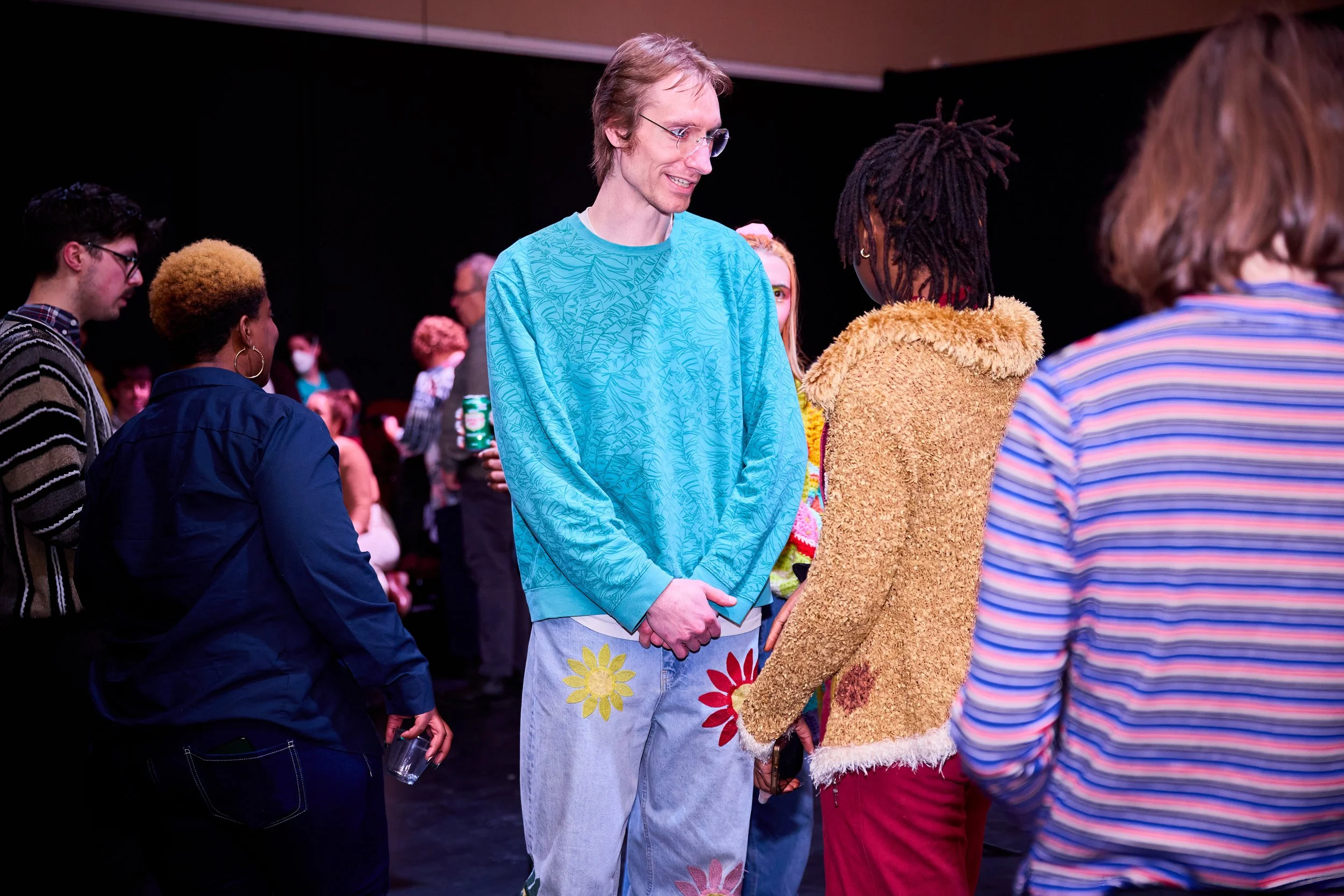 Groupe de personnes discutant lors d'un événement social, y compris un homme avec des vêtements colorés et des femmes en arrière-plan.