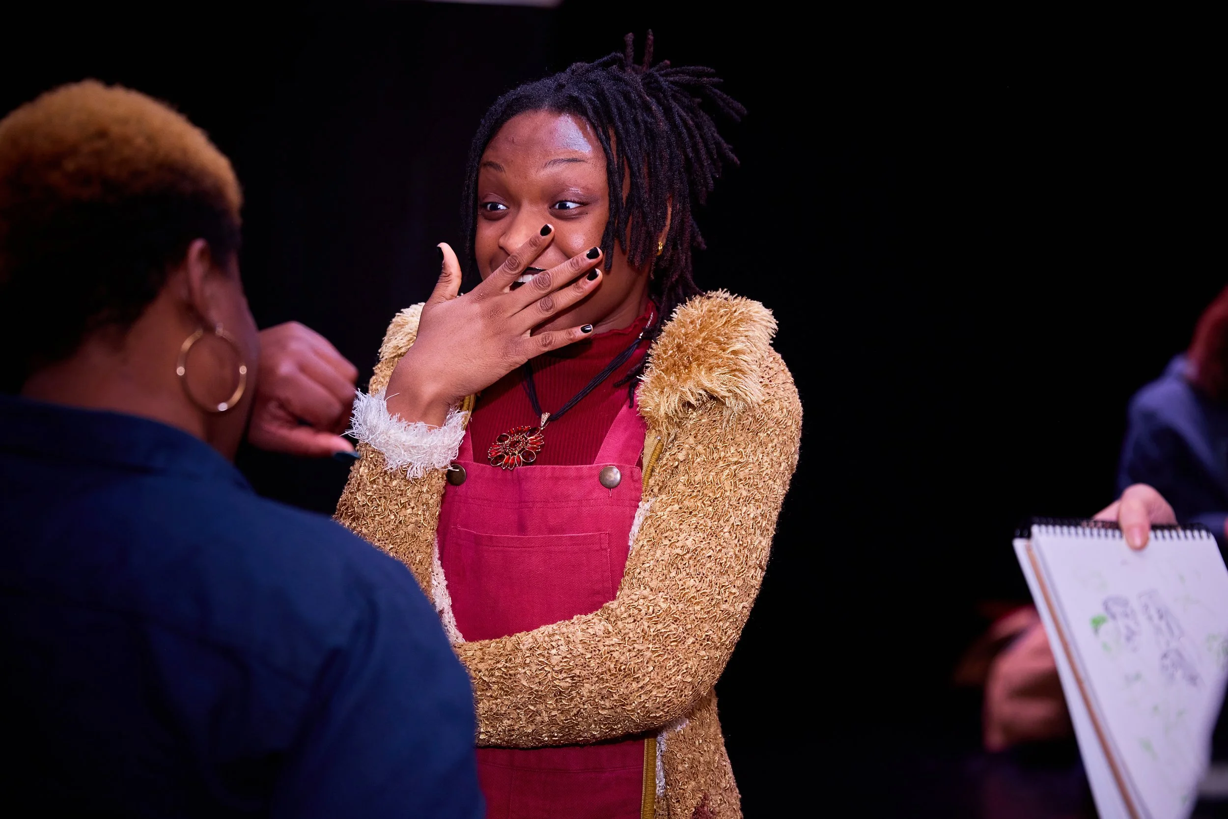 Deux femmes en conversation, l'une exprime une surprise ou une émotion en se touchant la bouche, l'autre est vue de dos, en détresse.