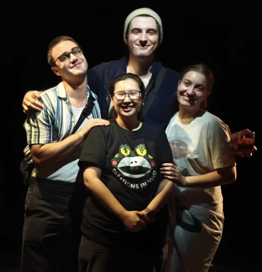 Cinq personnes souriantes posant ensemble en groupe, trois femmes et deux hommes, dans un fond noir. rotation de personnes en position décontractée et amicale.