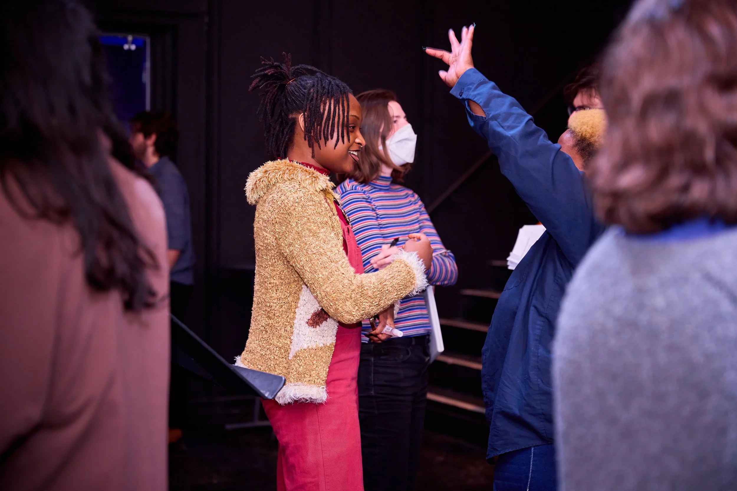Groupe de personnes discutant, une femme portant un manteau beige discute avec une autre femme avec un masque, dans un environnement intérieur