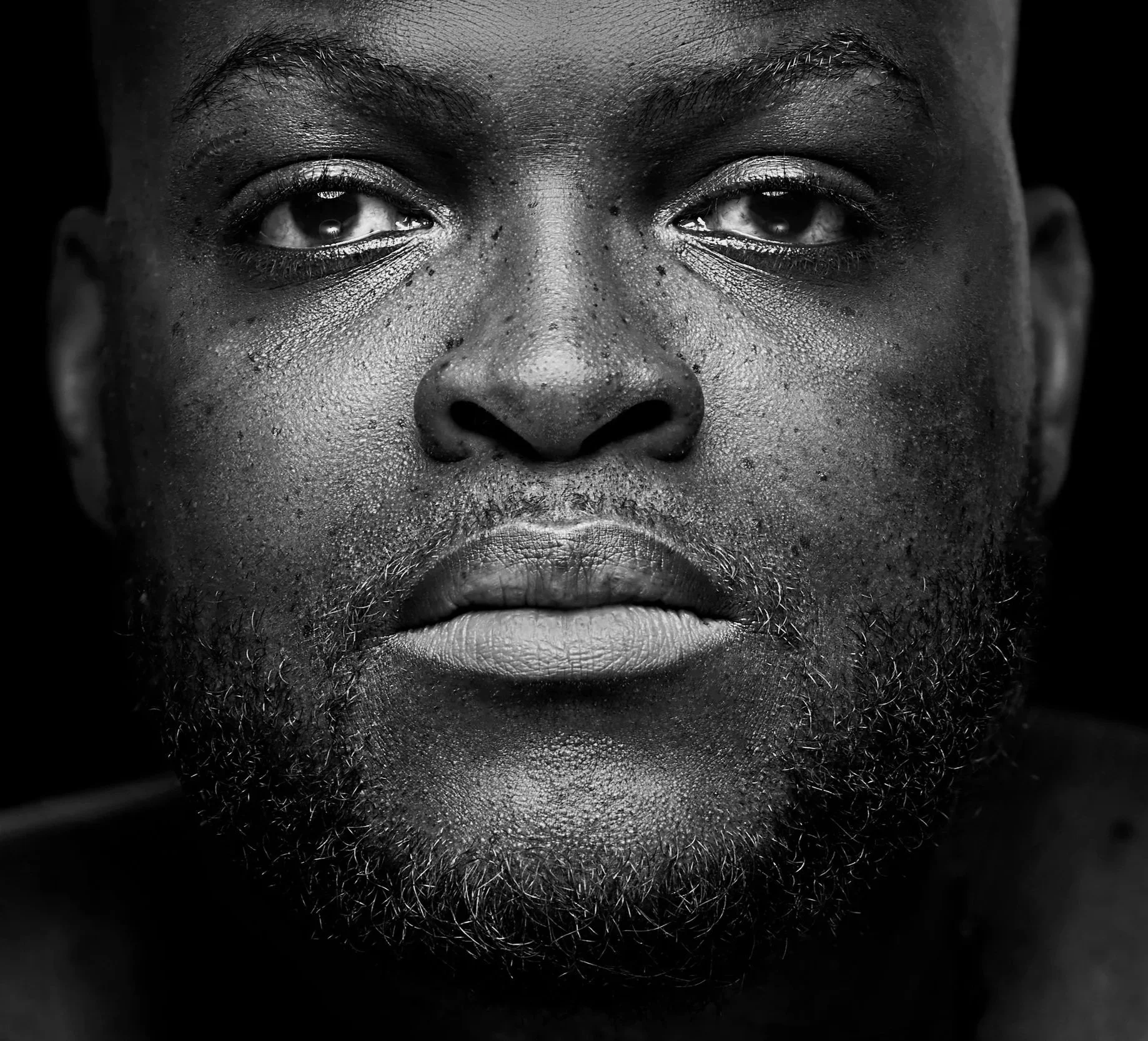 visage en gros plan d'un homme noir avec une peau humide, barbe et moustache, regard fixe