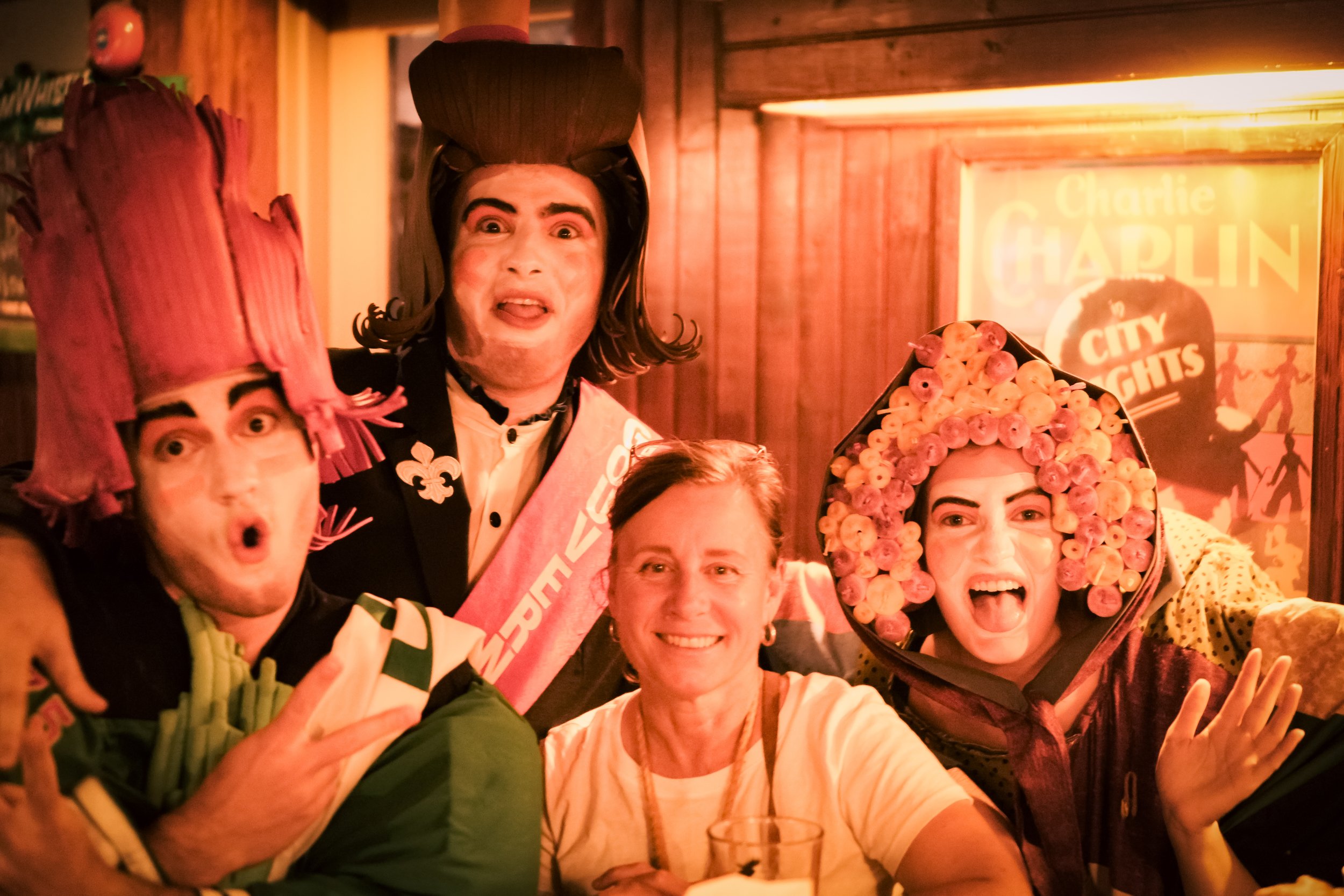 Créations In Vivo. Groupe de cinq personnes en costumes colorés, souriantes et joyeuses, posant pour une photo dans un lieu avec une décoration en bois.