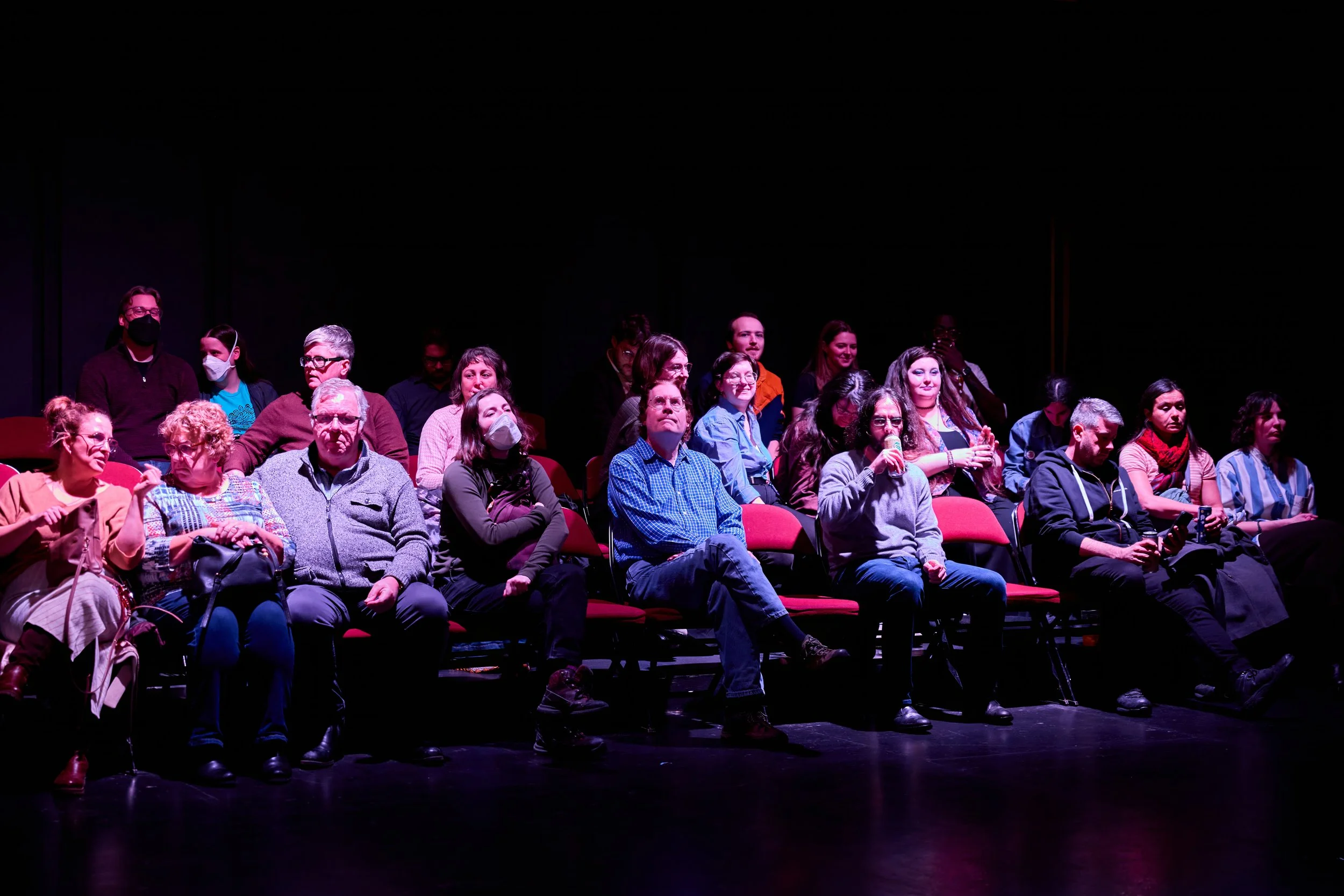 public réunissant des personnes assises dans une salle de spectacle, certaines portant un masque, sous un éclairage violet.