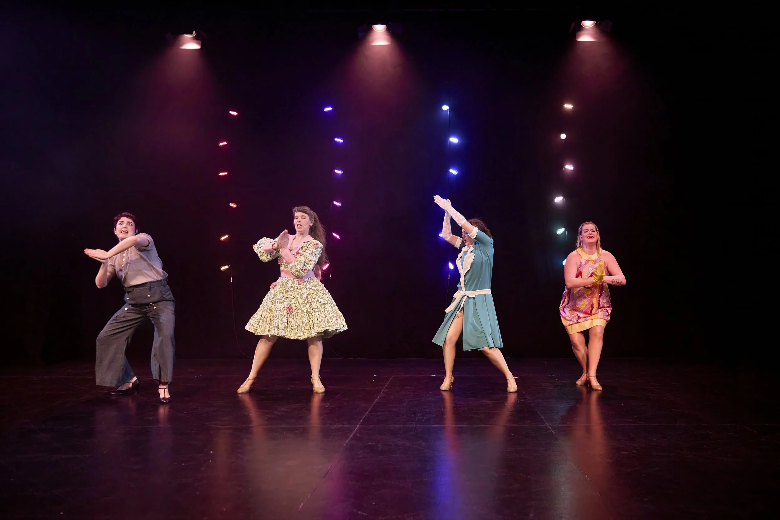 Créations In Vivo. Quatre femmes en costumes colorés dansant sur scène avec des lumières colorées en arrière-plan.