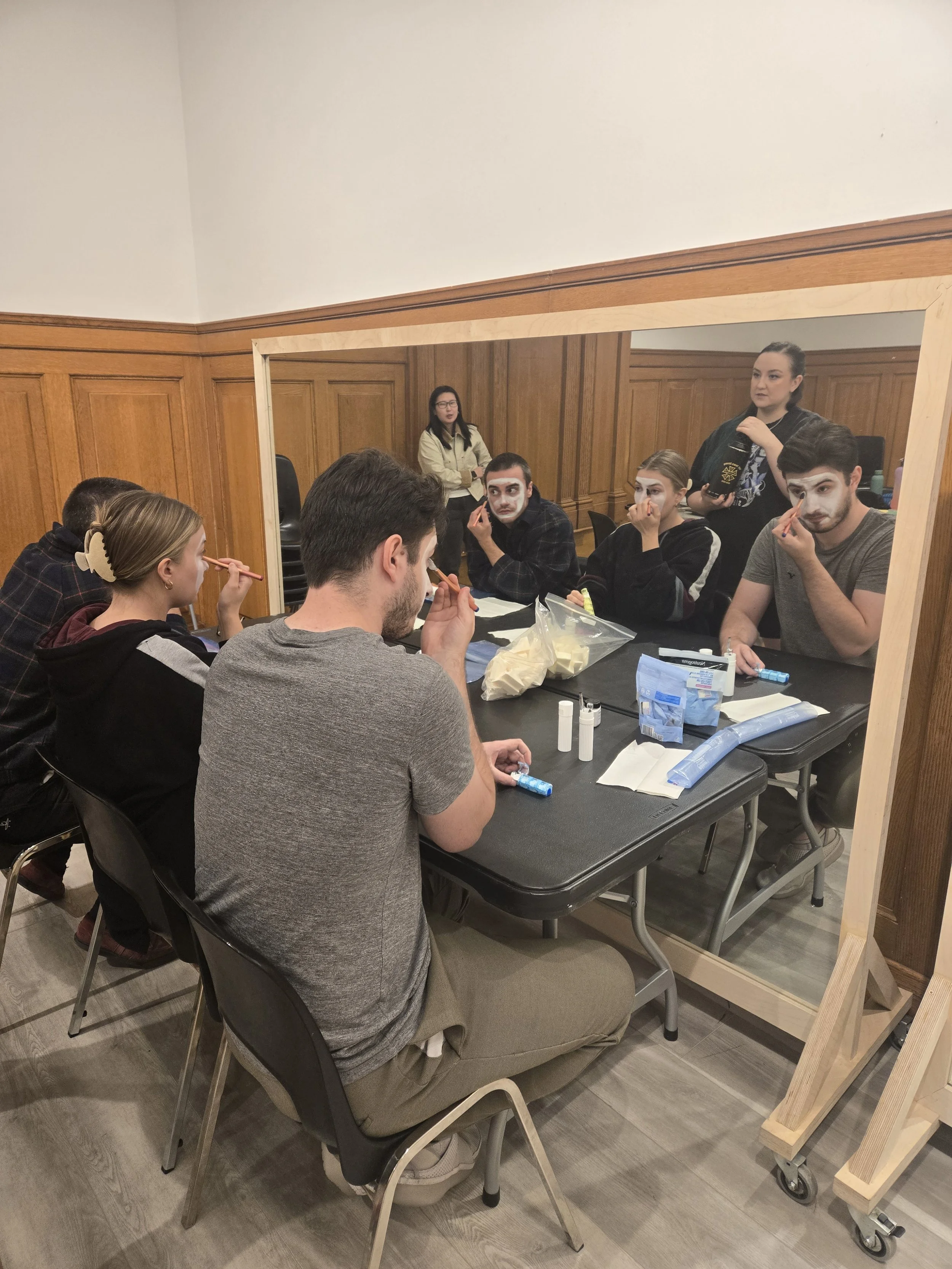 Créations In Vivo. Groupe de jeunes adultes maquillés en préparation pour une pièce de théâtre ou un événement artistique, vus à travers une vitre.