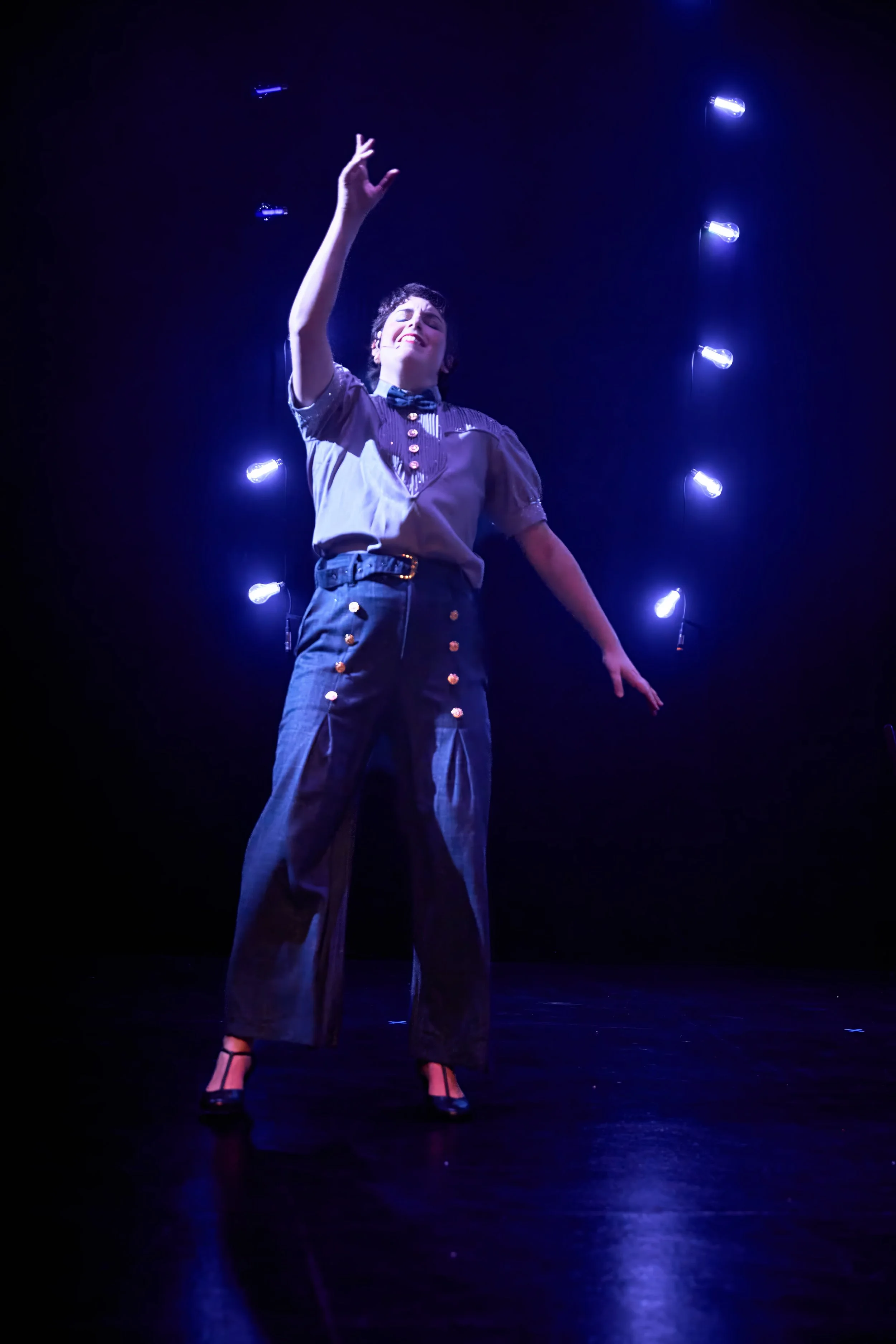 Une femme en costume rétro se produisant sur scène sous un éclairage violet, avec des néons bleus en arrière-plan.
