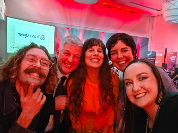 Créations In Vivo. Cinq personnes souriantes posent pour une selfie dans une salle avec éclairage rouge, ambiance festive.