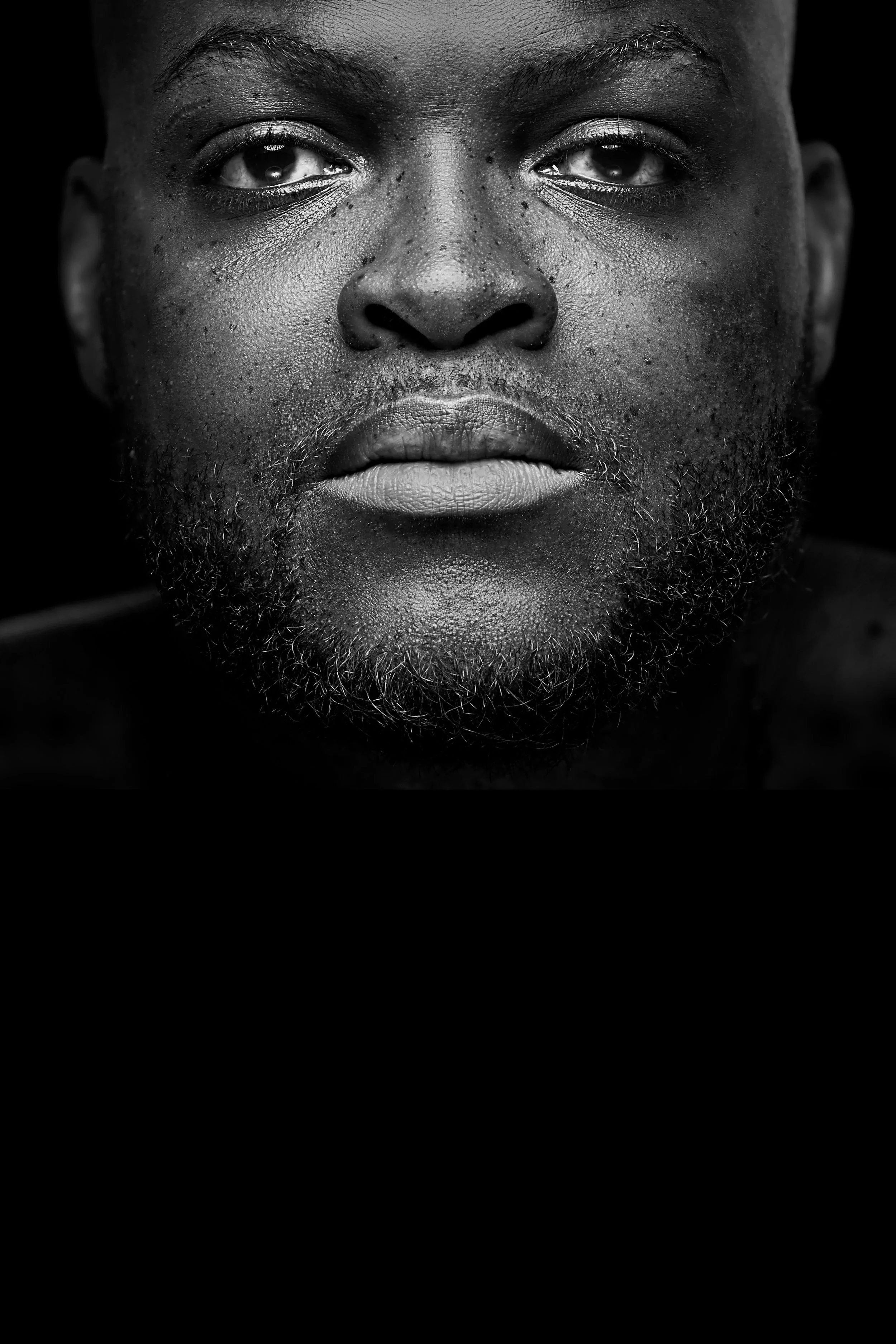 Yao. Portrait en noir et blanc d'un homme Noir avec une barbe, regardant directement l'objectif, expression neutre, détails du visage visibles.