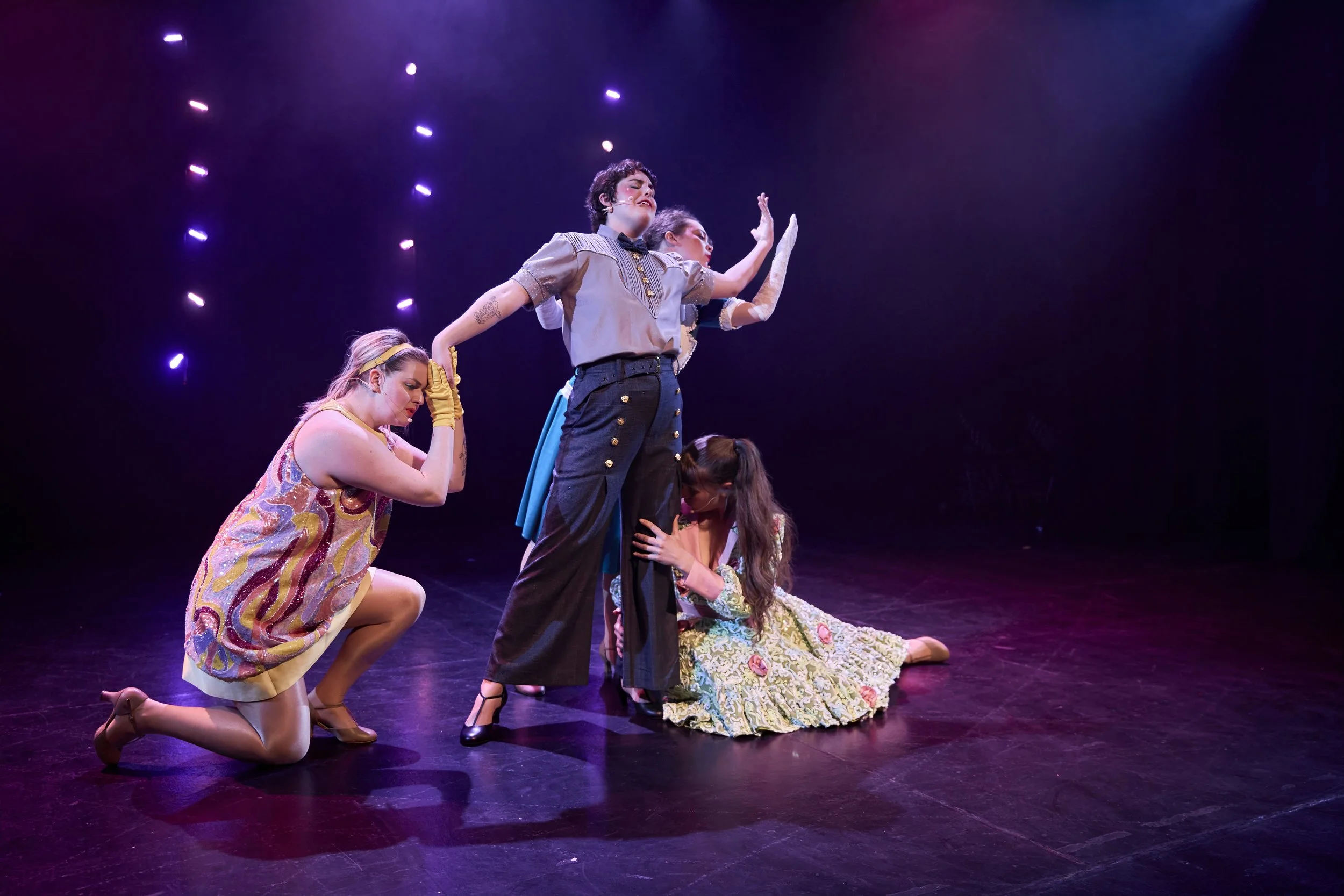 Quatre femmes en costume de théâtre dans une scène dramatique sur scène avec des lumières violettes.