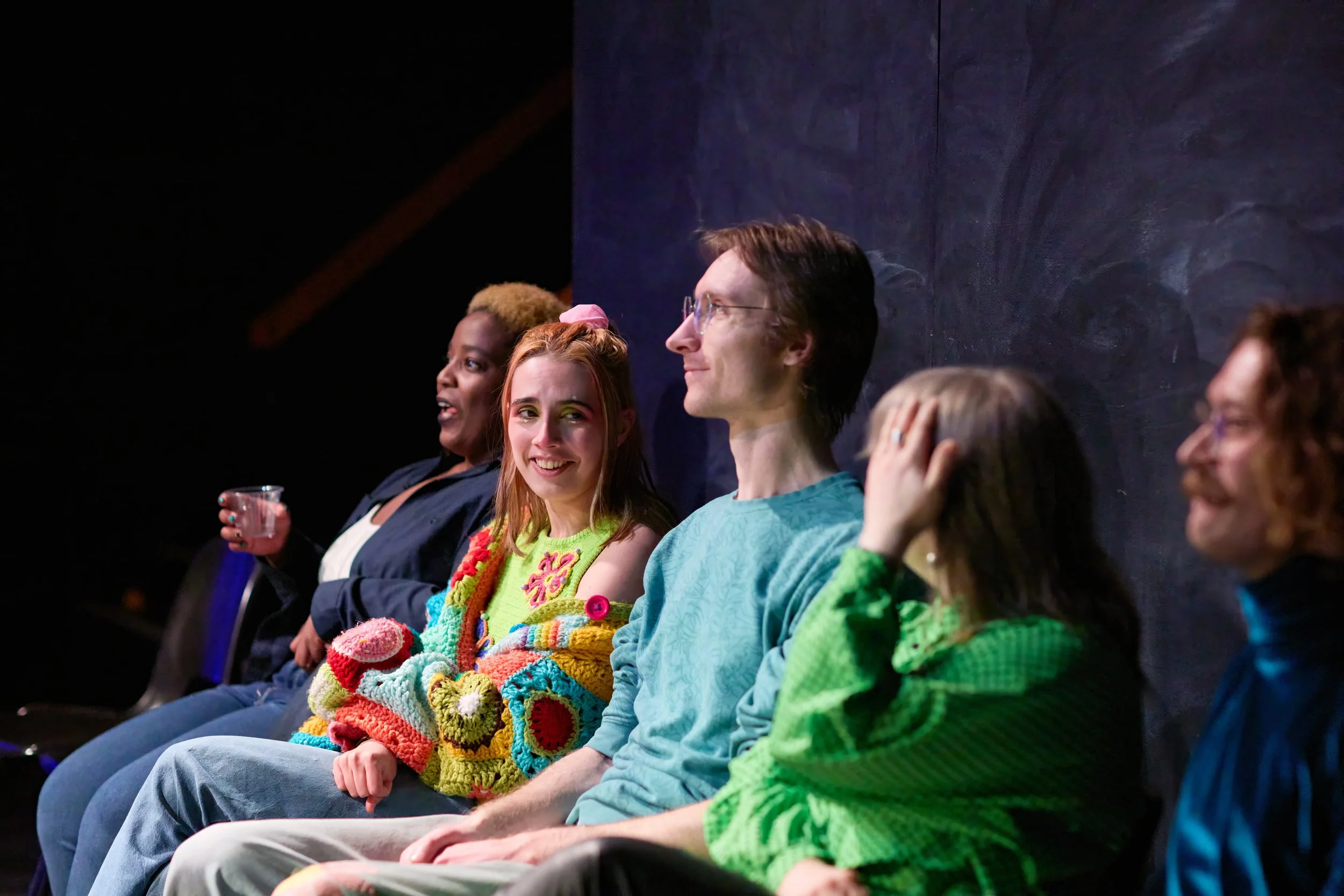 Groupe de cinq personnes assises côte à côte, discutant et souriant dans un environnement intérieur.