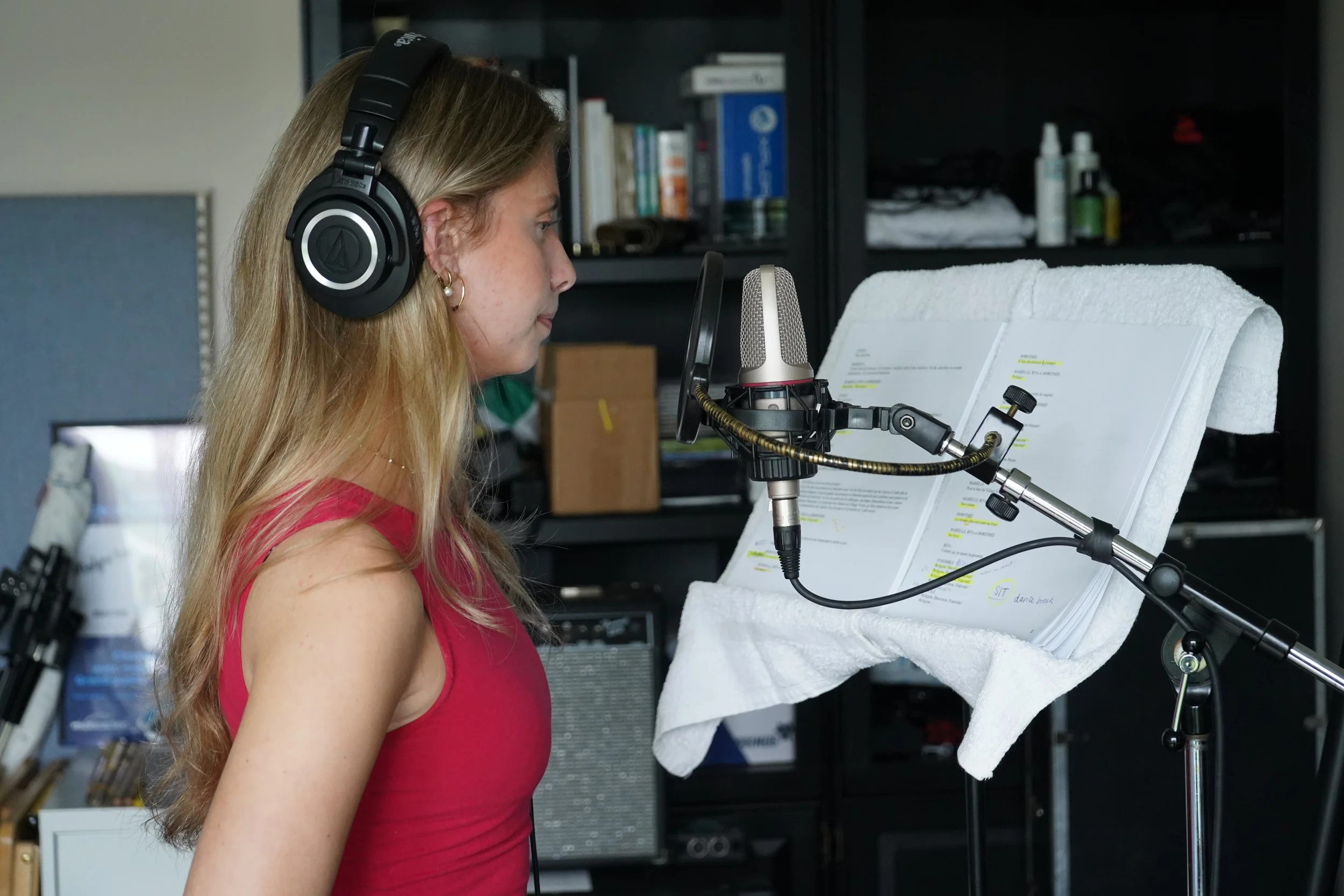 Femme en studio d'enregistrement, portant un casque audio, lisant une partition musicale sur un support en mousse, avec un microphone devant elle.