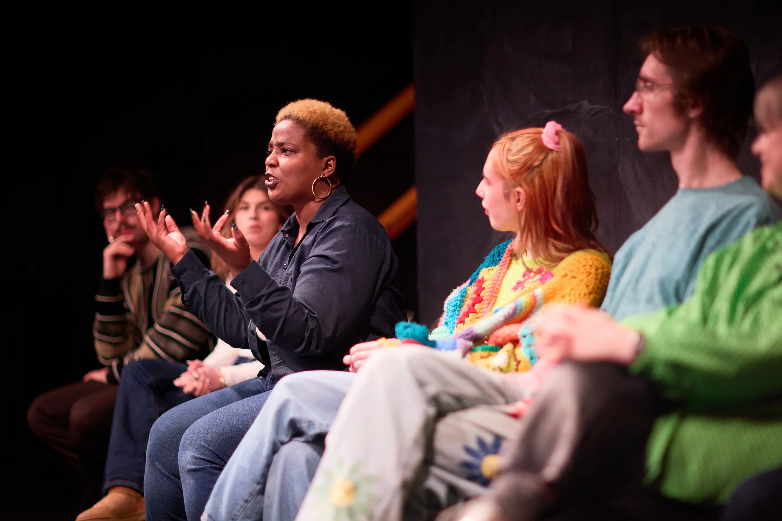 Groupe de personnes en discussion lors d'une réunion ou spectacle, la femme au centre parle avec expressivité.