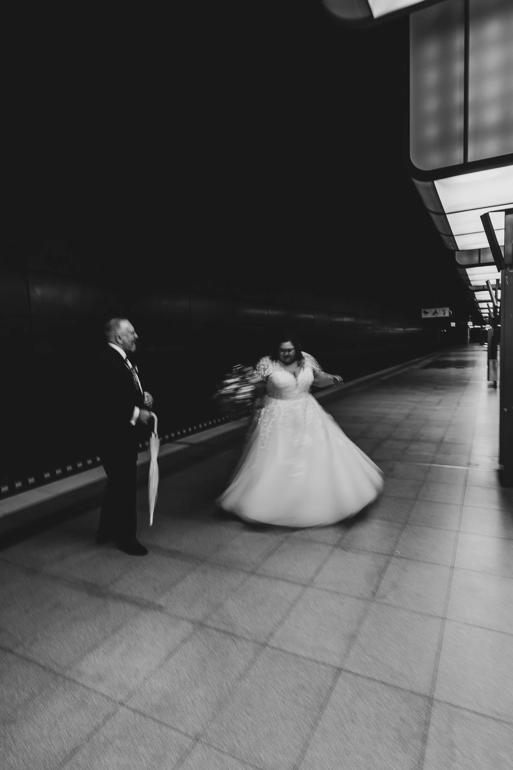 Braut in Hochzeitskleid tanzt mit Bräutigam in einem dunklen, leeren Bahnhof.