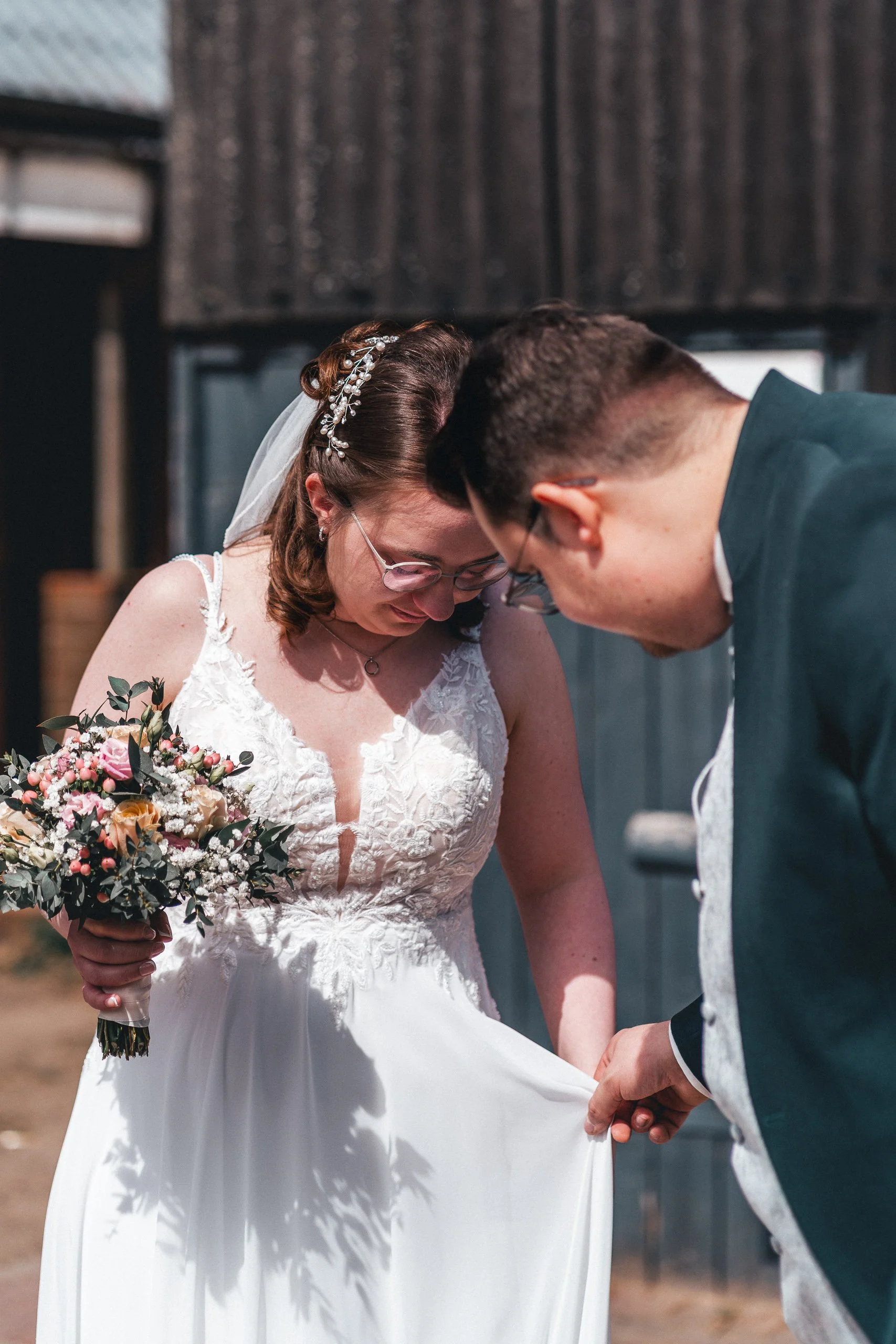 Ein Brautpaar bei einer Hochzeitszeremonie, die Hände der beiden halten sich, die Braut trägt ein weißes Hochzeitskleid und hält einen Blumenstrauß, der Bräutigam trägt einen dunklen Anzug.