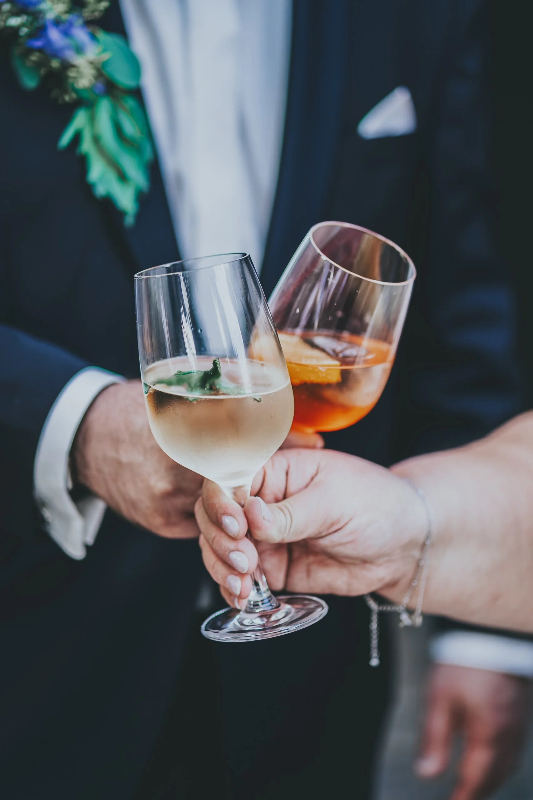 Zwei Menschen, die elegante Gläser mit Wein anstoßen. Einer trägt einen schwarzen Anzug mit weißem Hemd, der andere einen dunklen Anzug. Es handelt sich wahrscheinlich um eine festliche Gelegenheit.