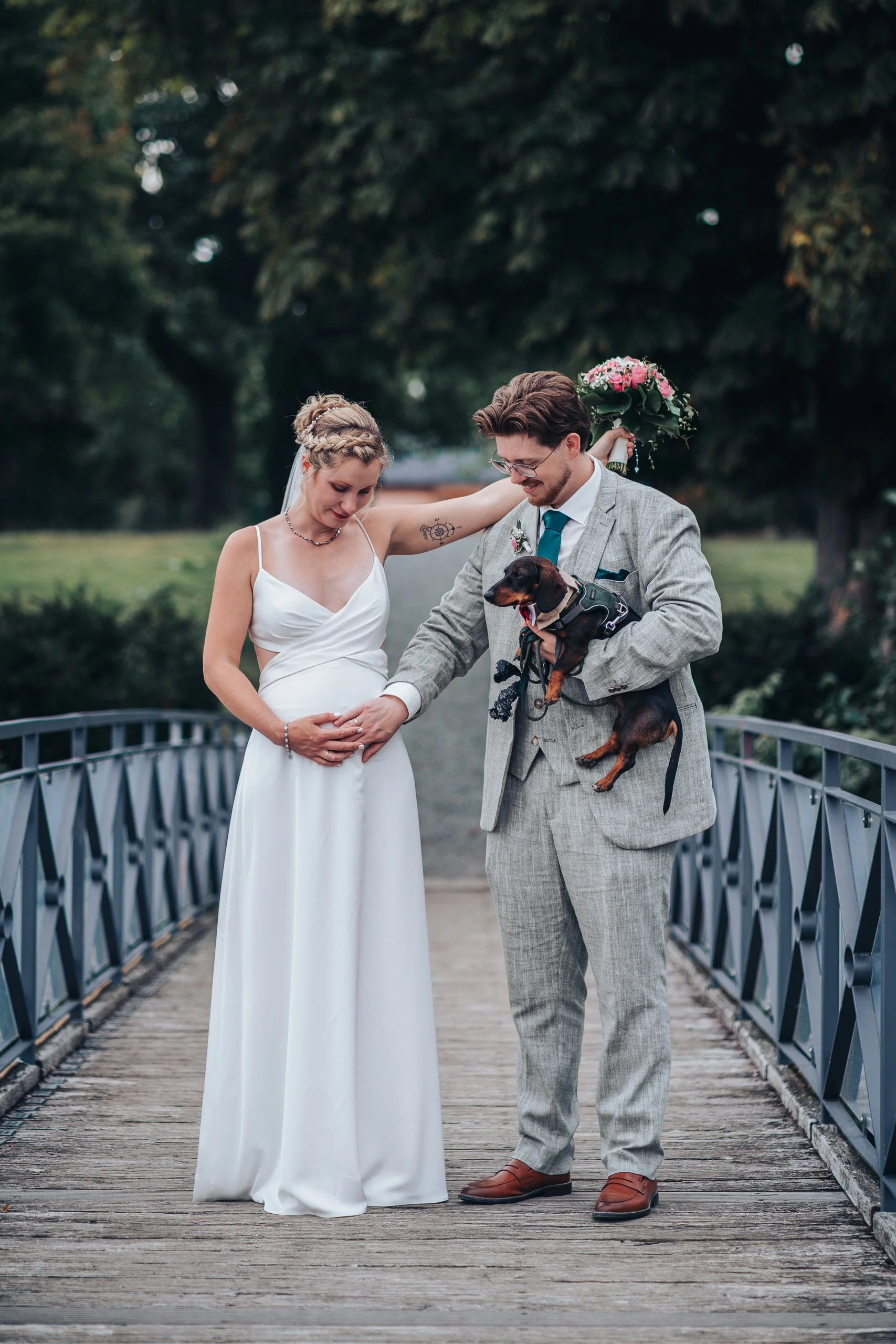 Brautpaar mit Hund auf einer Brücke im Grünen.