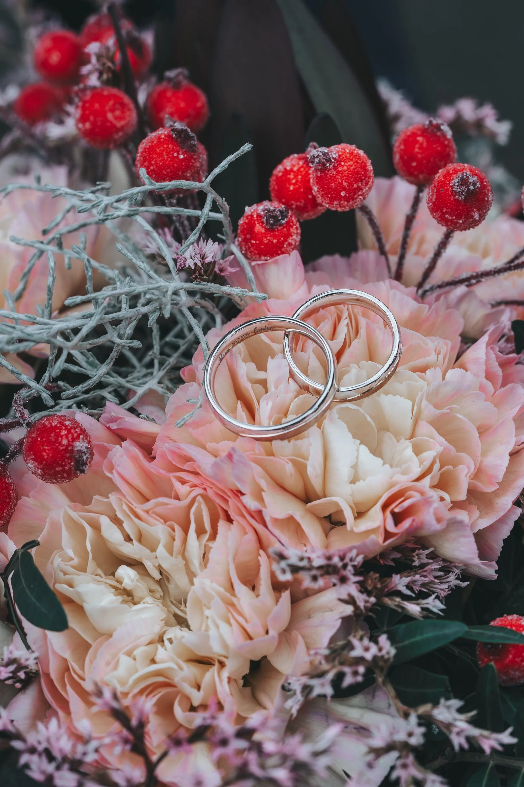 Trauringe auf dem Brautstrauß mit winterlichen Details und roten Beeren.