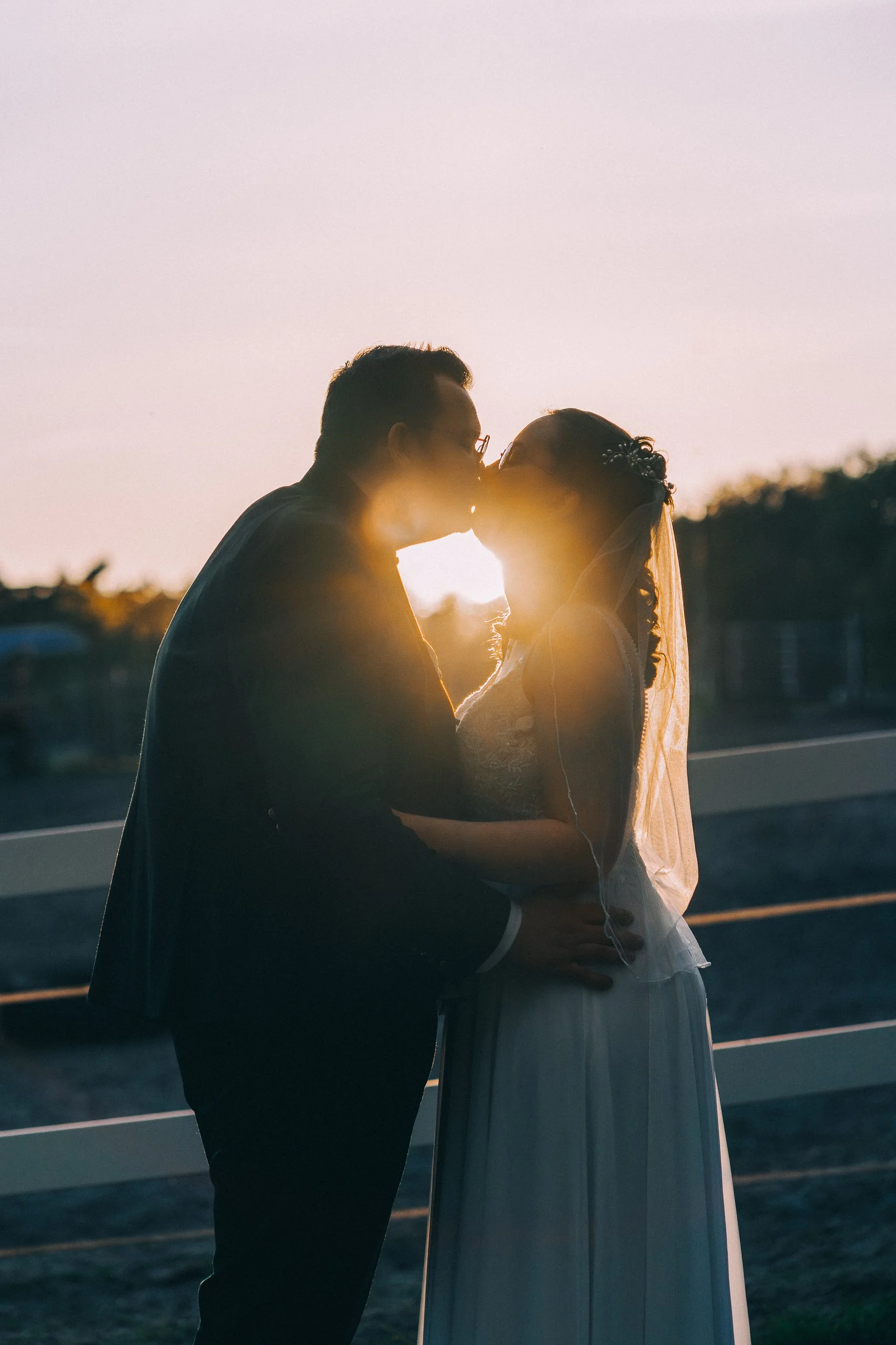 Braut und Bräutigam küssen sich bei Sonnenuntergang, romantische Stimmung, Heiratszeremonie im Freien.