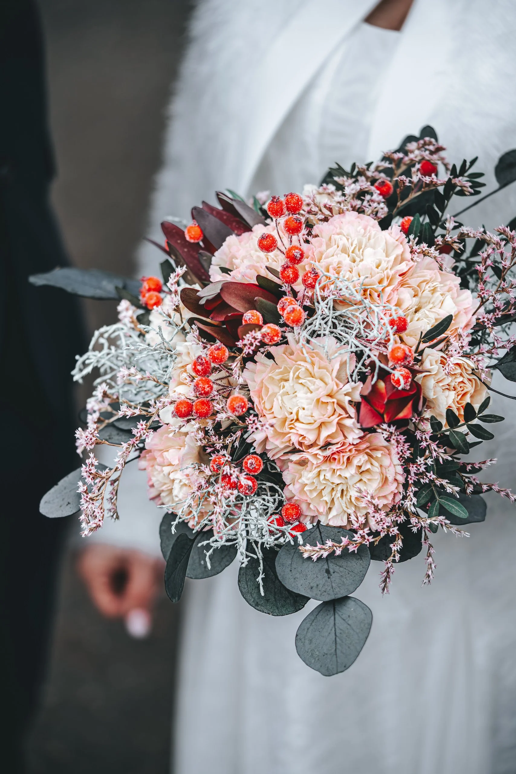 Winterlicher Brautstrauß mit roten Beeren, Eukalyptus und zarten Blüten, Detailaufnahme.