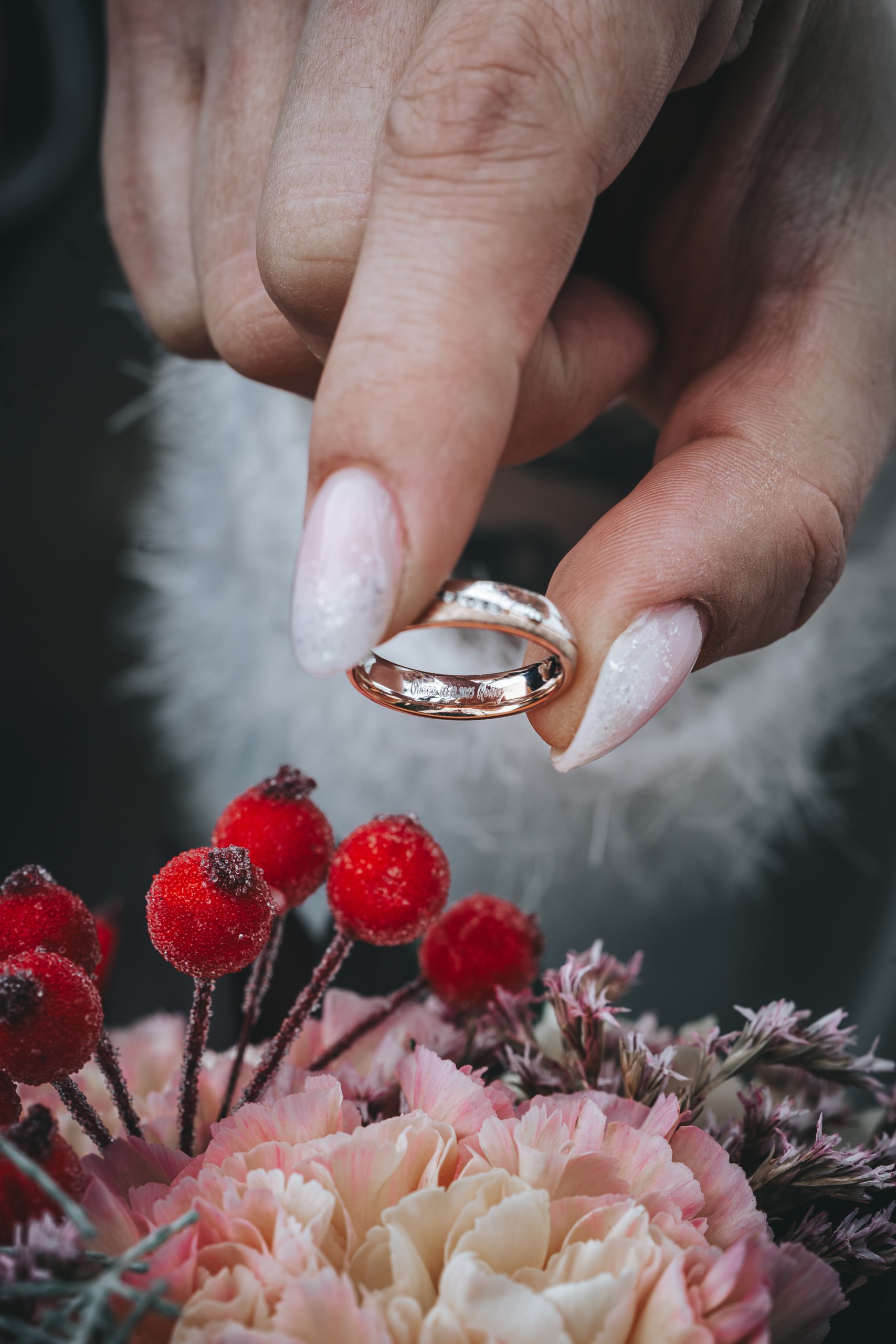 Trauring mit Gravur in der Hand, darunter Brautstrauß mit roten Beeren.