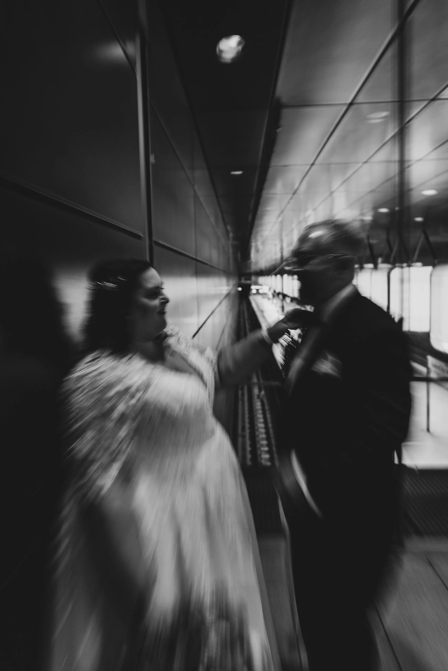 Schwarz-weiß-Foto von einem Konflikt zwischen einem Mann und einer Frau in einem modernen Gebäude mit reflektierenden Wänden.