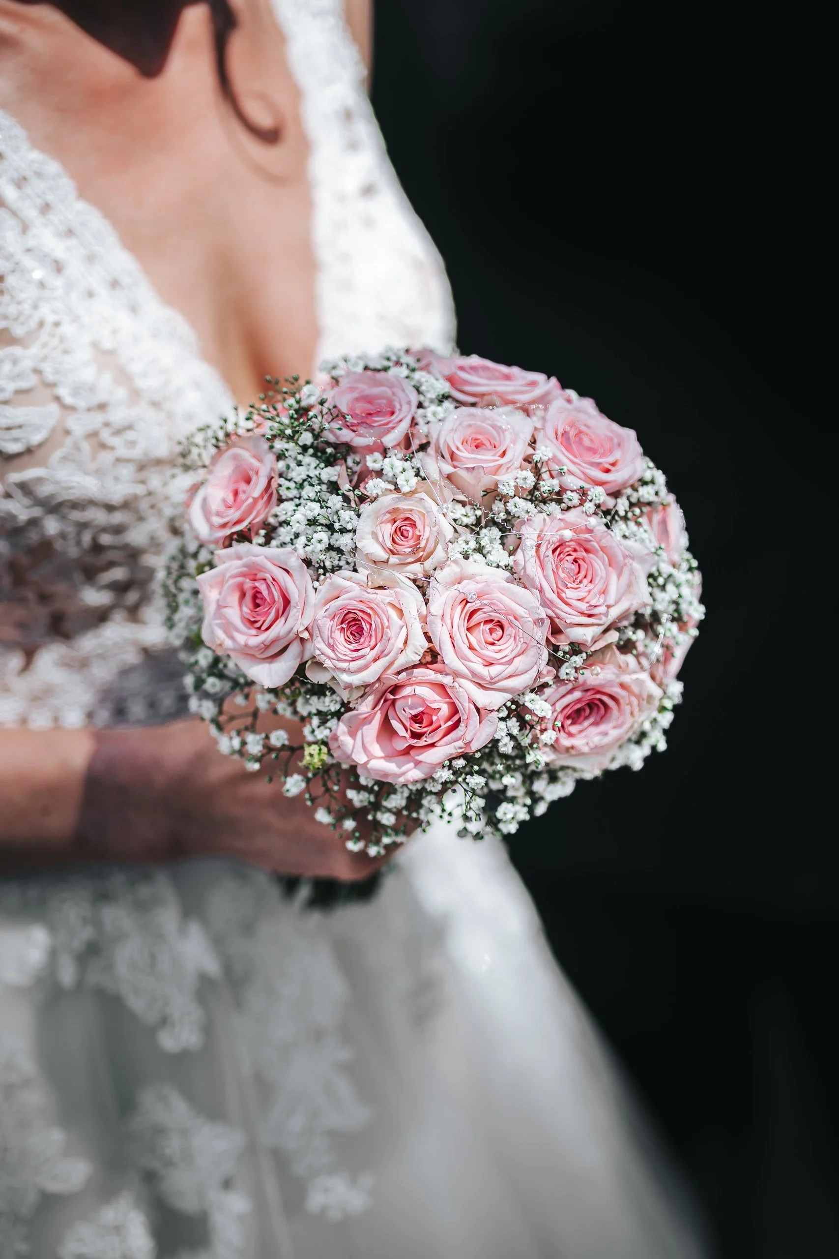 Der Braut hält einen Blumenstrauß aus pinken Rosen und kleinen weißen Blümchen.