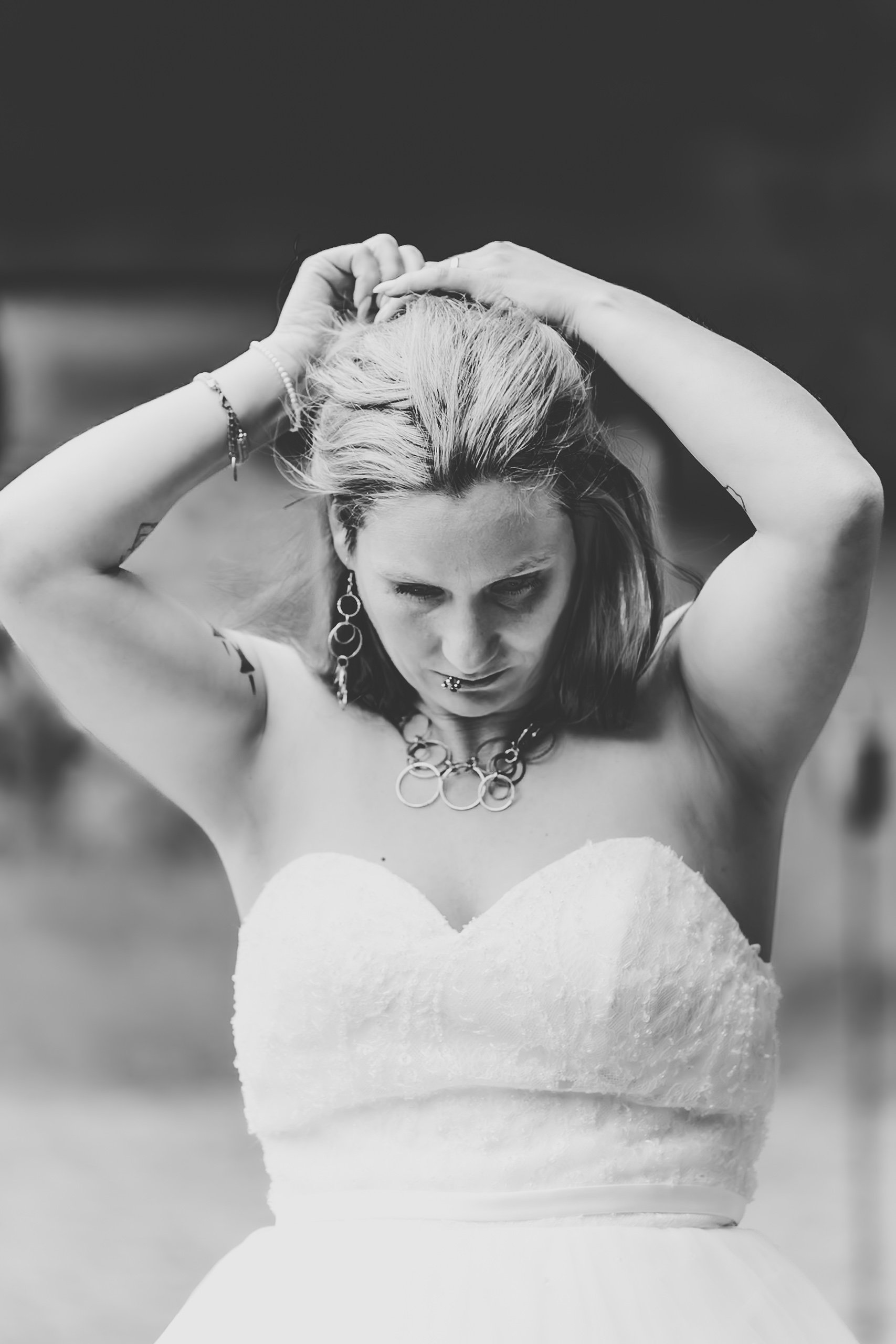 Schwarz-weiß-Foto einer Frau in einem Brautkleid, die die Haare hochgesteckt hat und nach unten schaut, während sie ihre Arme hebt.