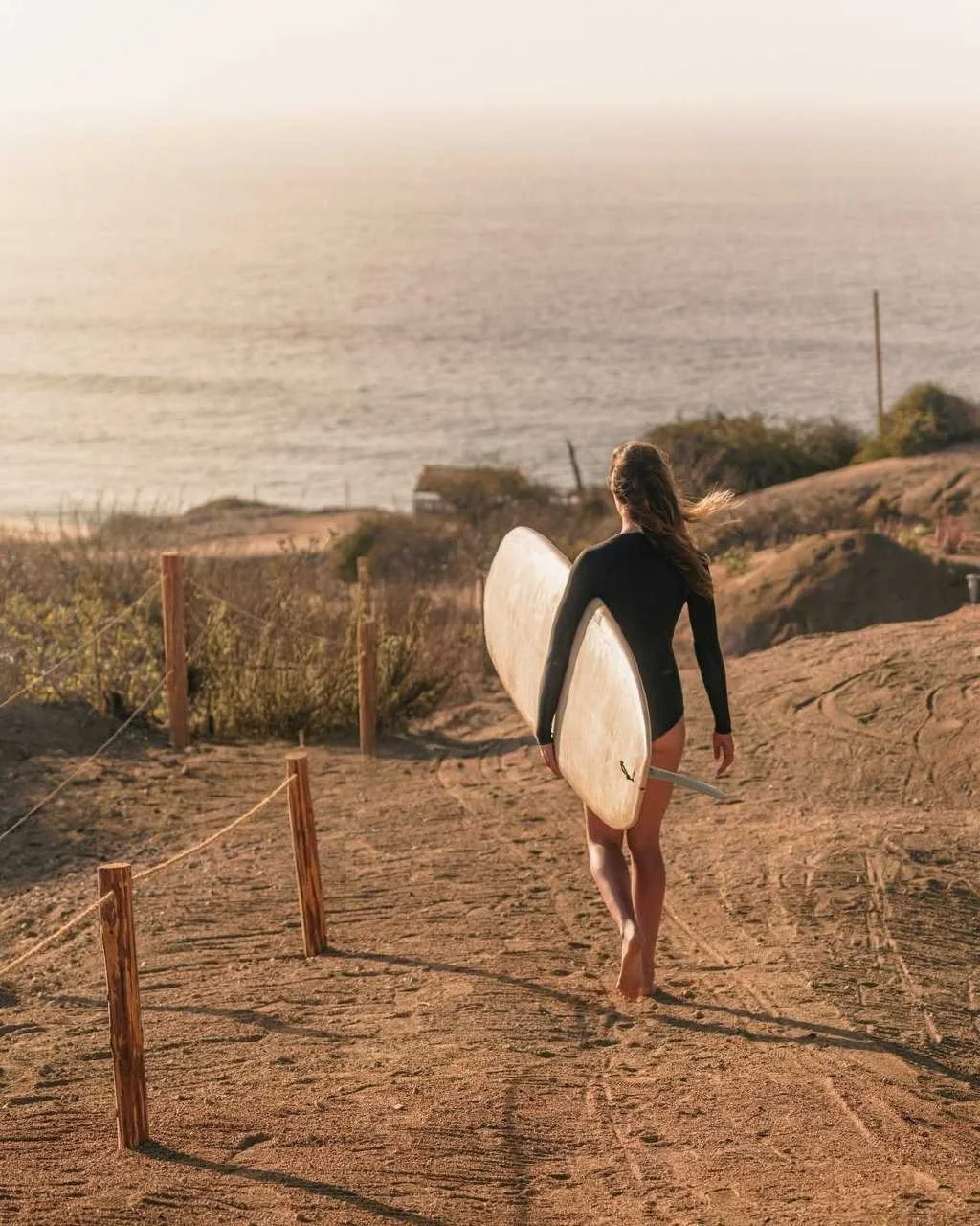 Person carrying surfboard toward beach at sunset