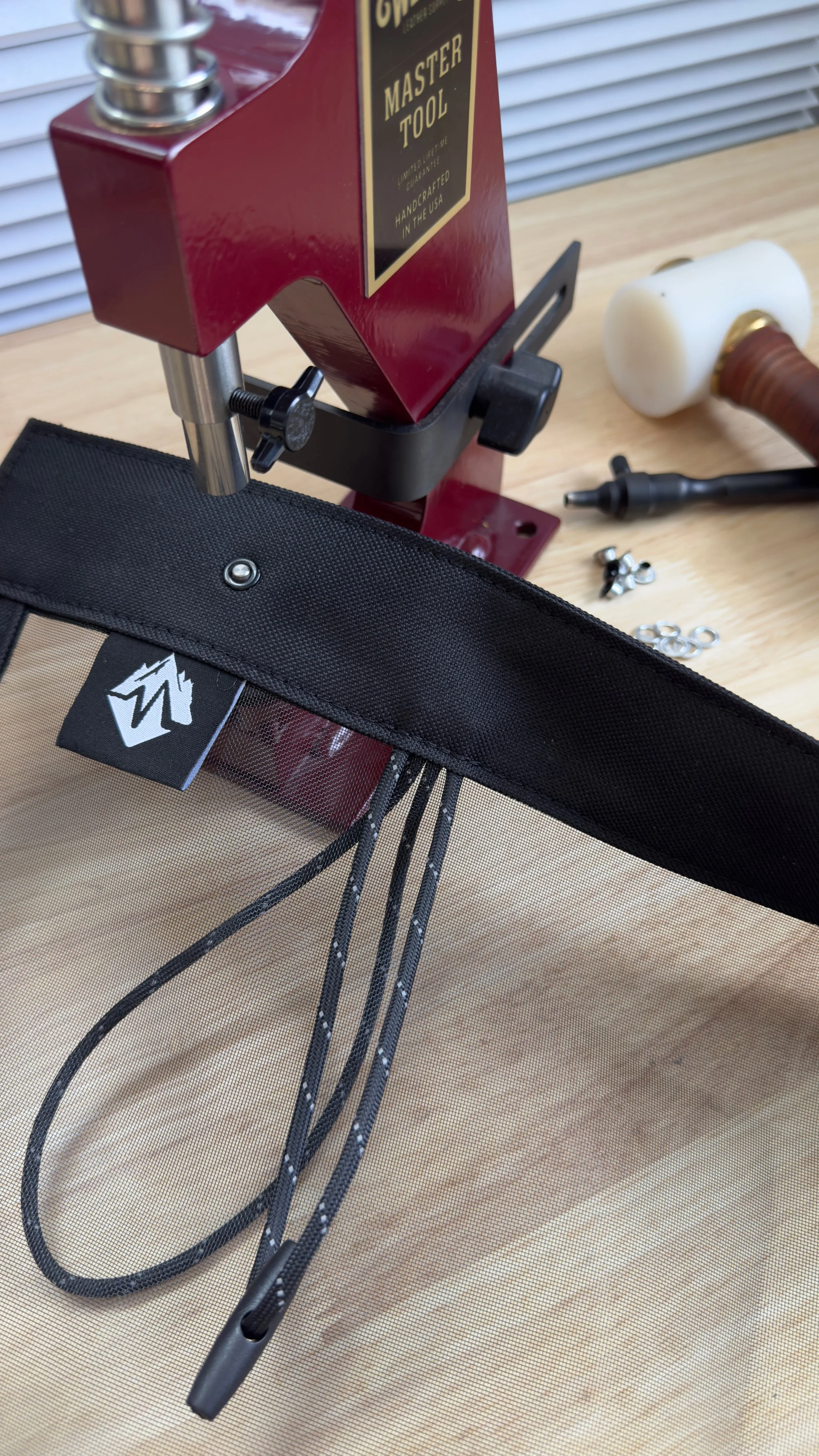 Close-up of a rear bug screen for a Tune Outdoors camper with the Made for Wheelers logo. Grommets are being installed to the screen that are used to mount to the Tune camper. Toggle ties are used to tie the screen when not in use.