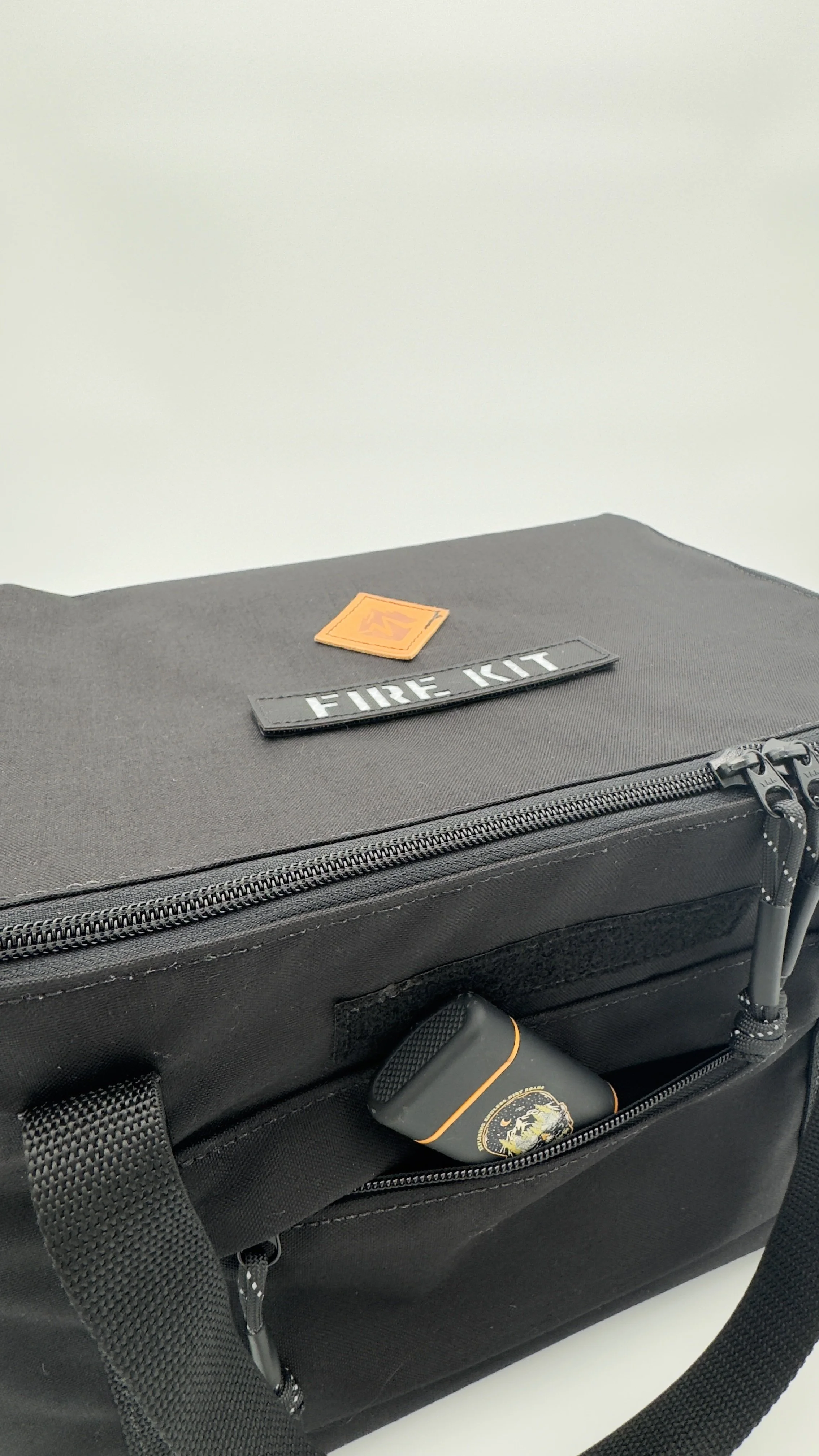 Black emergency fire kit bag with a small rectangular container with an emergency symbol inside a front pocket