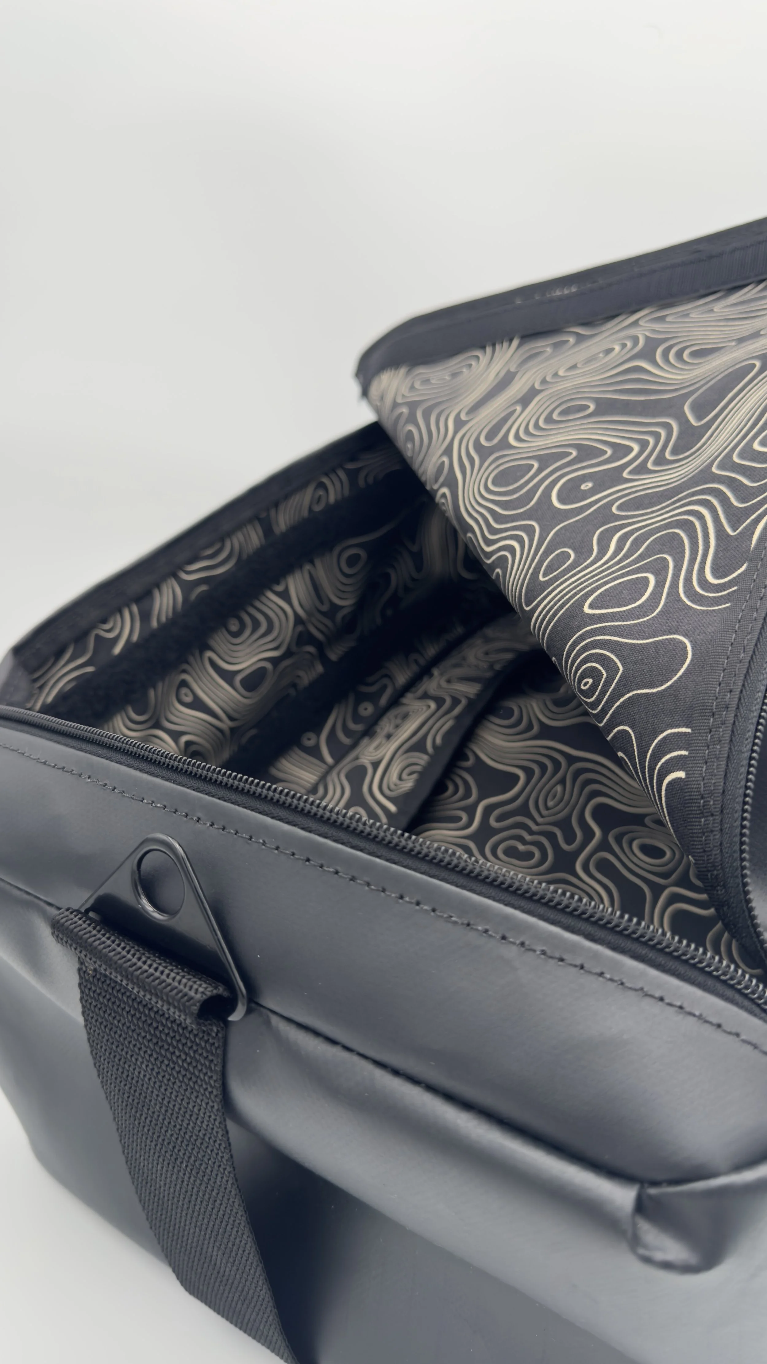 Open black travel or toiletry bag with a patterned interior, showing multiple compartments and a zipper closure.