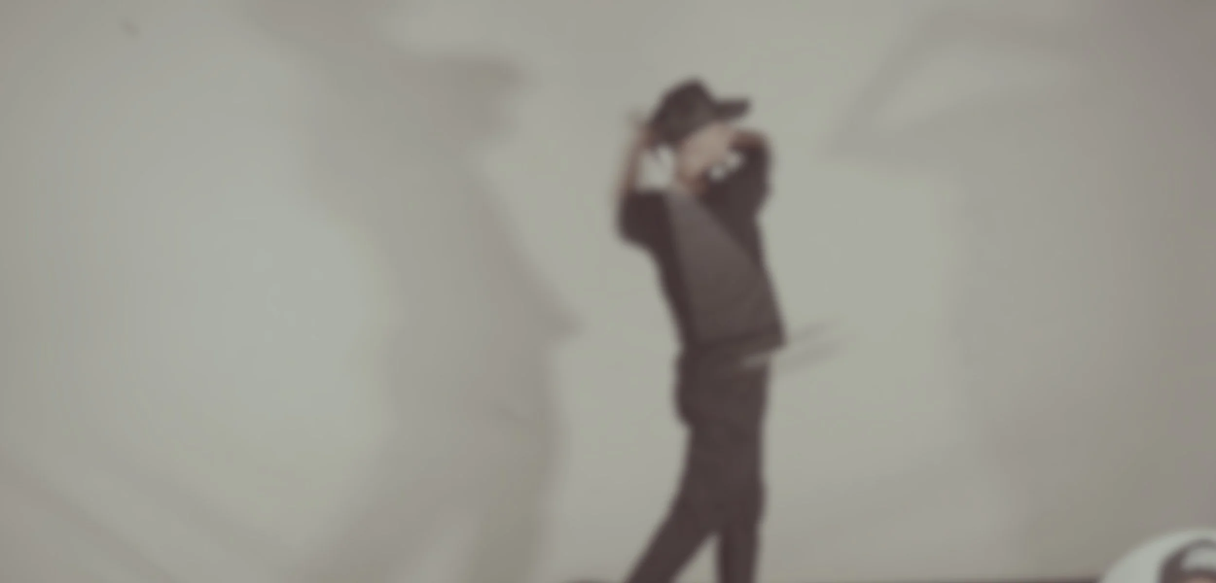 Person standing against a plain wall, wearing dark clothing, with one hand on their head and the other resting on their arm, in a contemplative pose.