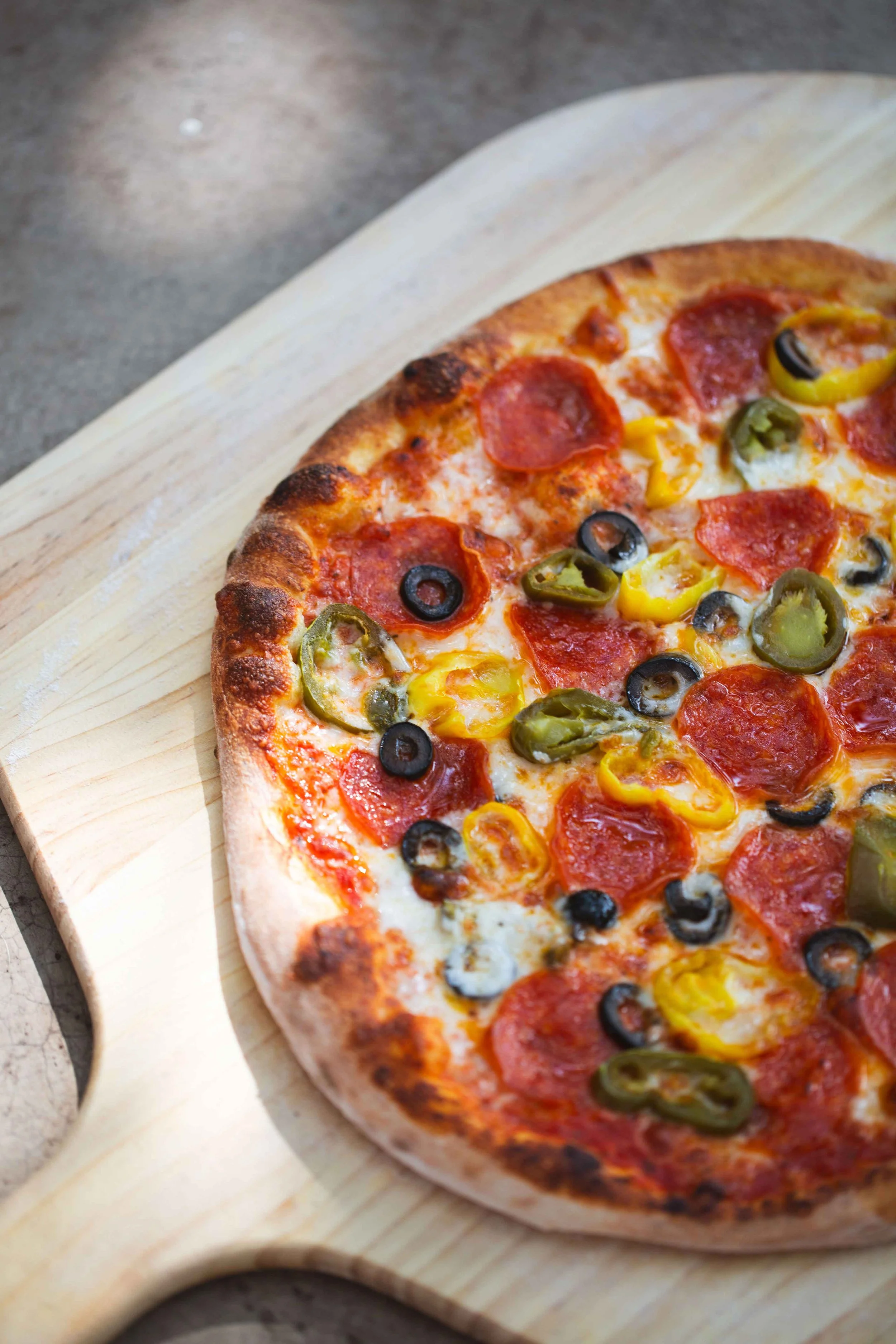 Pizza with pepperoni, black olives, green peppers, yellow peppers, and cheese on a wooden paddle