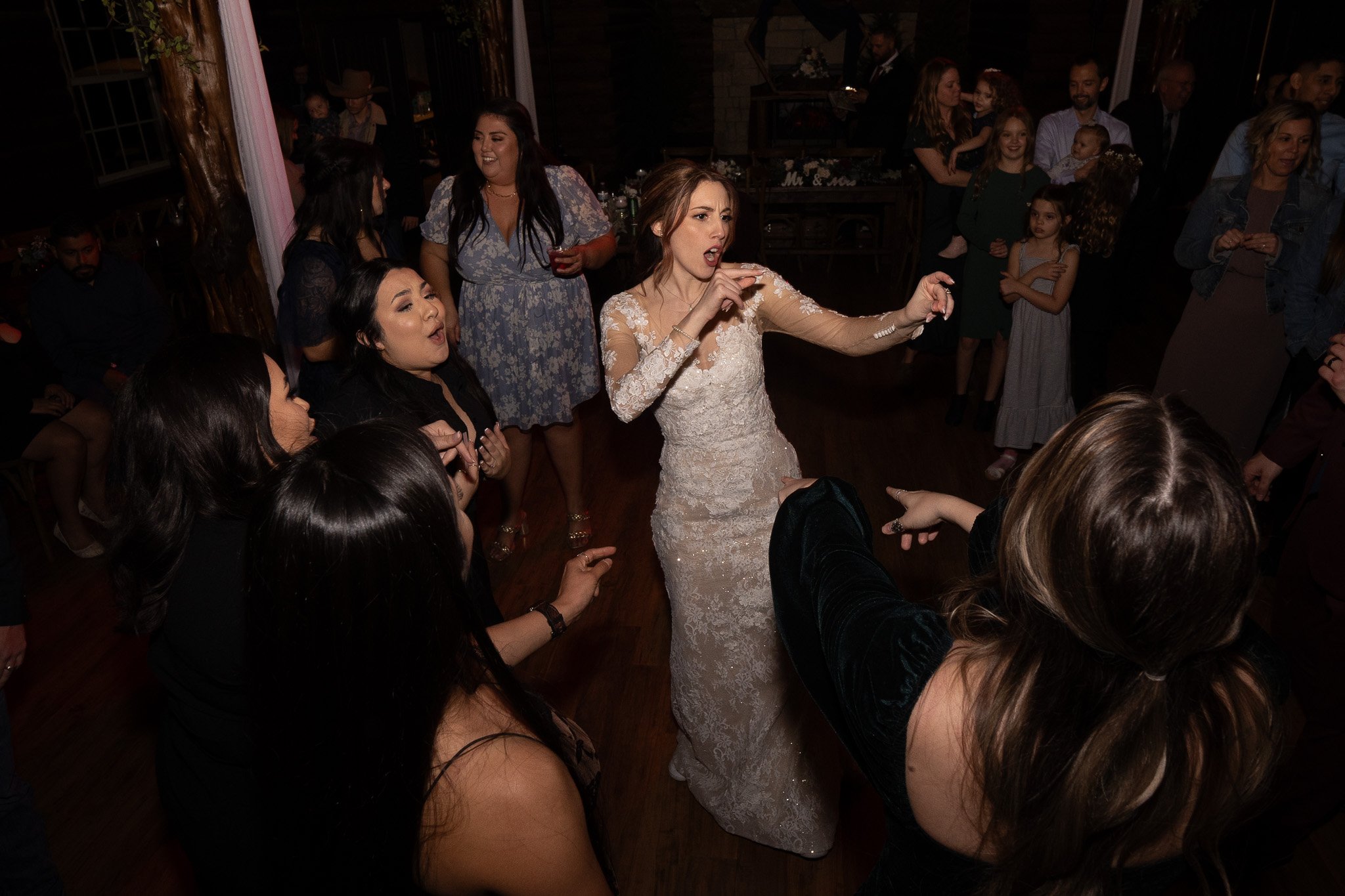 Women dancing and celebrating at a wedding reception, with a bride in a white wedding gown at the center