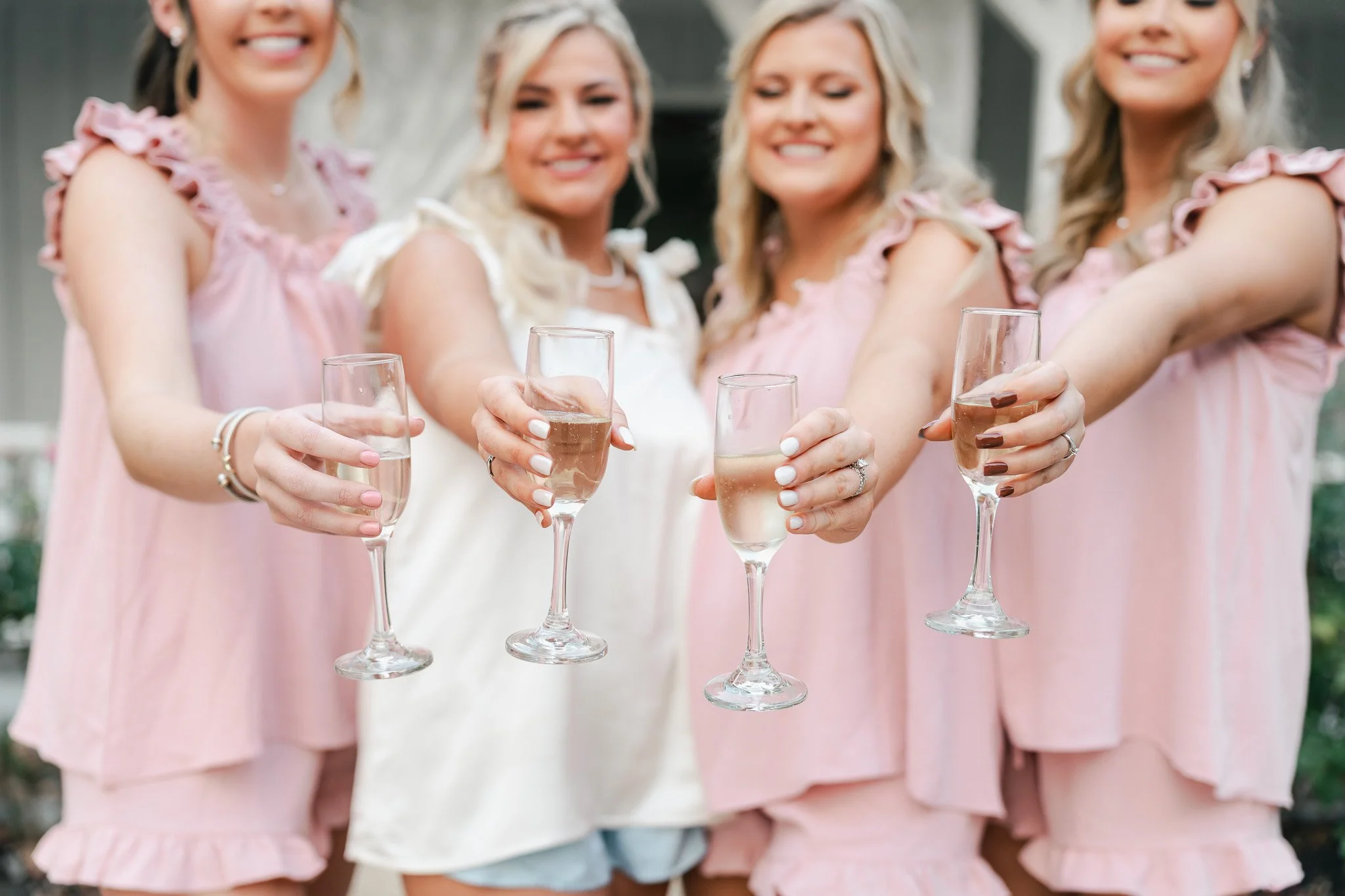 Four women dressed in pink and white dresses holding champagne glasses.