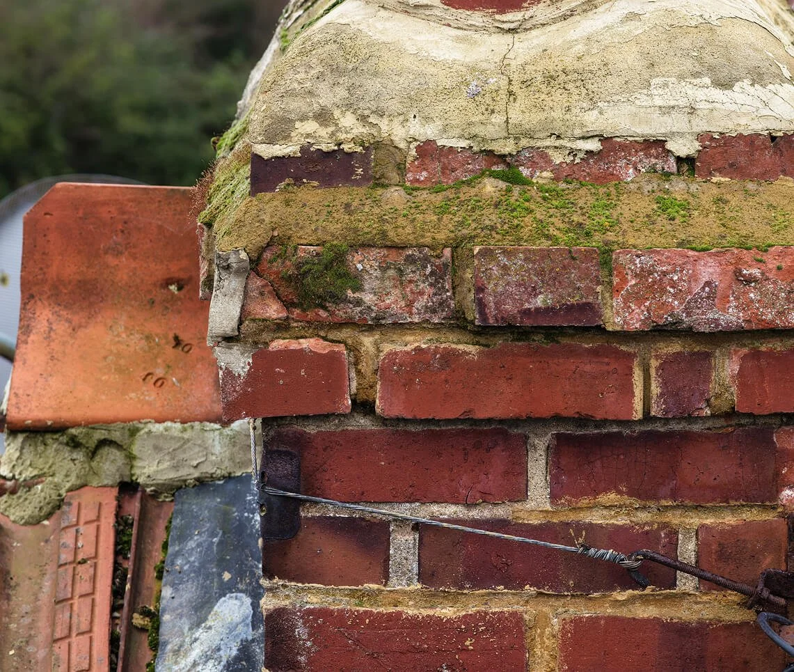 A chimney stack that is in a poor state with missing mortar and vegetation growth
