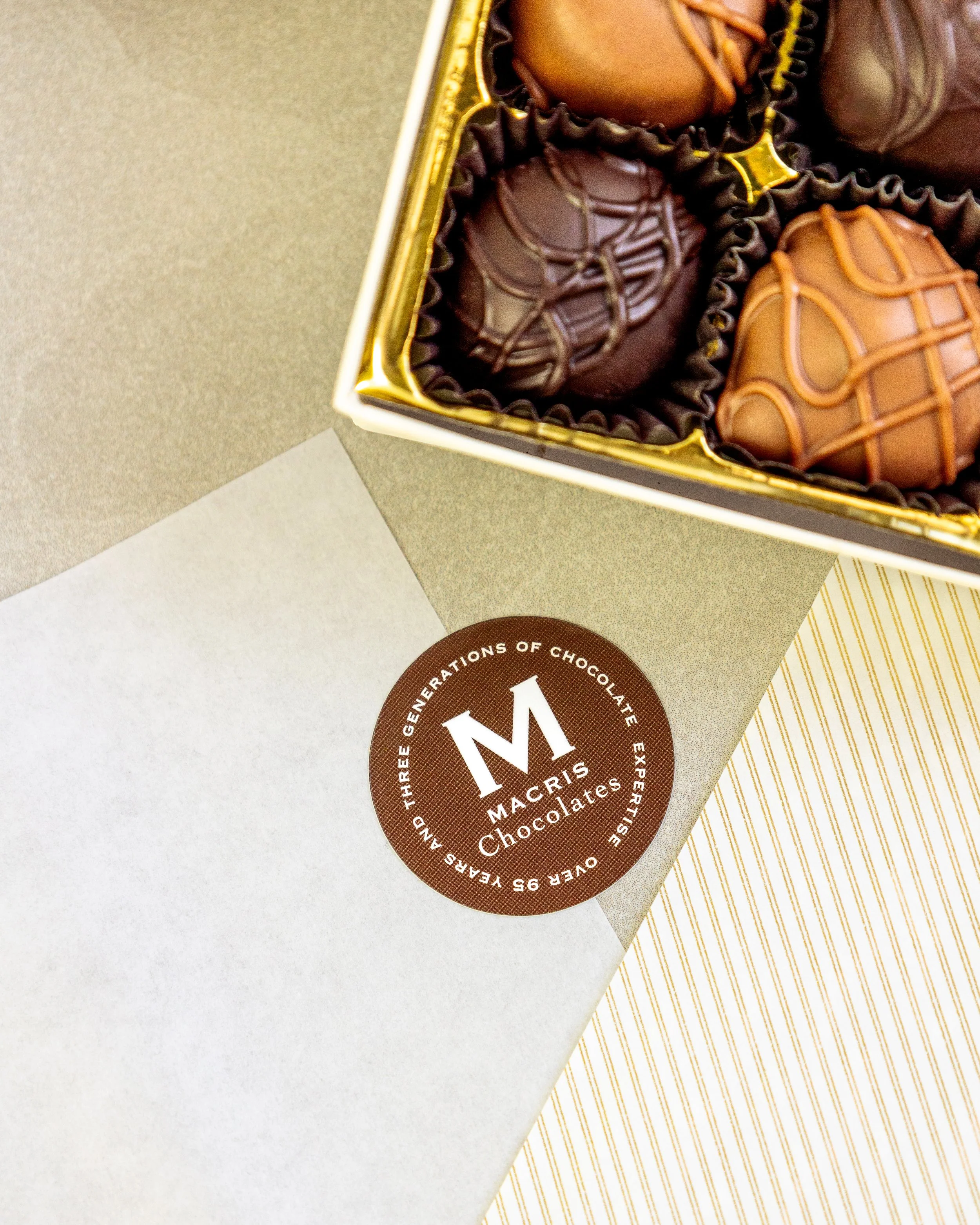 Product photography featuring assorted Macris Chocolates bars and boxed chocolates styled on neutral surfaces, highlighting packaging details, chocolate textures, and brand presentation in a clean, minimal, and classic setting.