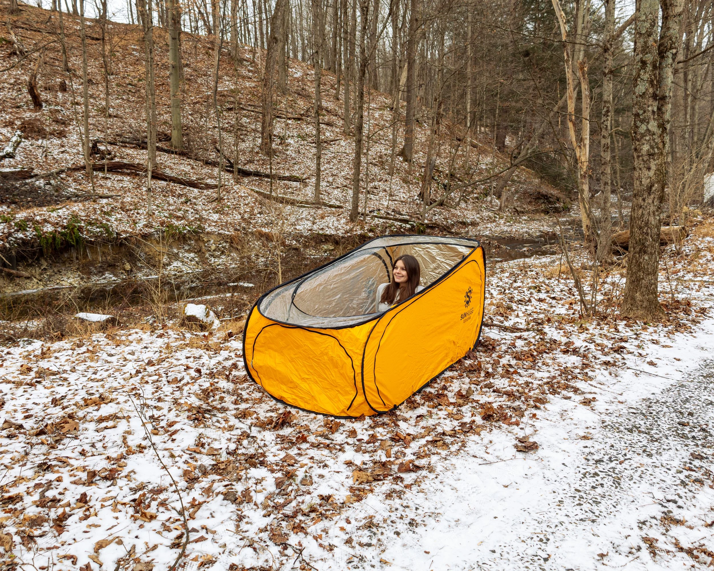 Lifestyle product photography featuring the SunHugg pop-up outdoor shelter, captured in a natural winter setting. Images highlight real-world use, setup and breakdown, interior details, branding elements, and scale to demonstrate functionality, porta