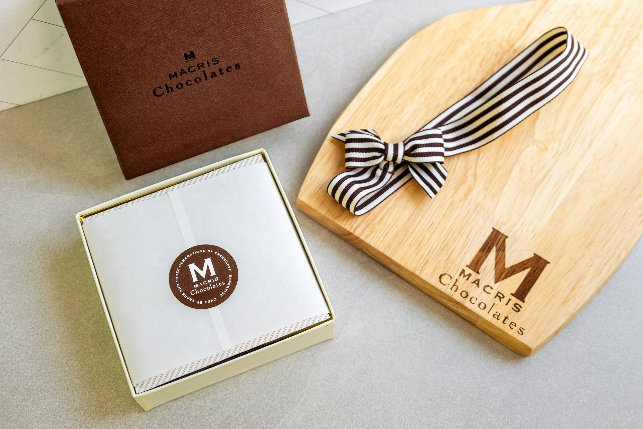 Product photography featuring assorted Macris Chocolates bars and boxed chocolates styled on neutral surfaces, highlighting packaging details, chocolate textures, and brand presentation in a clean, minimal, and classic setting.