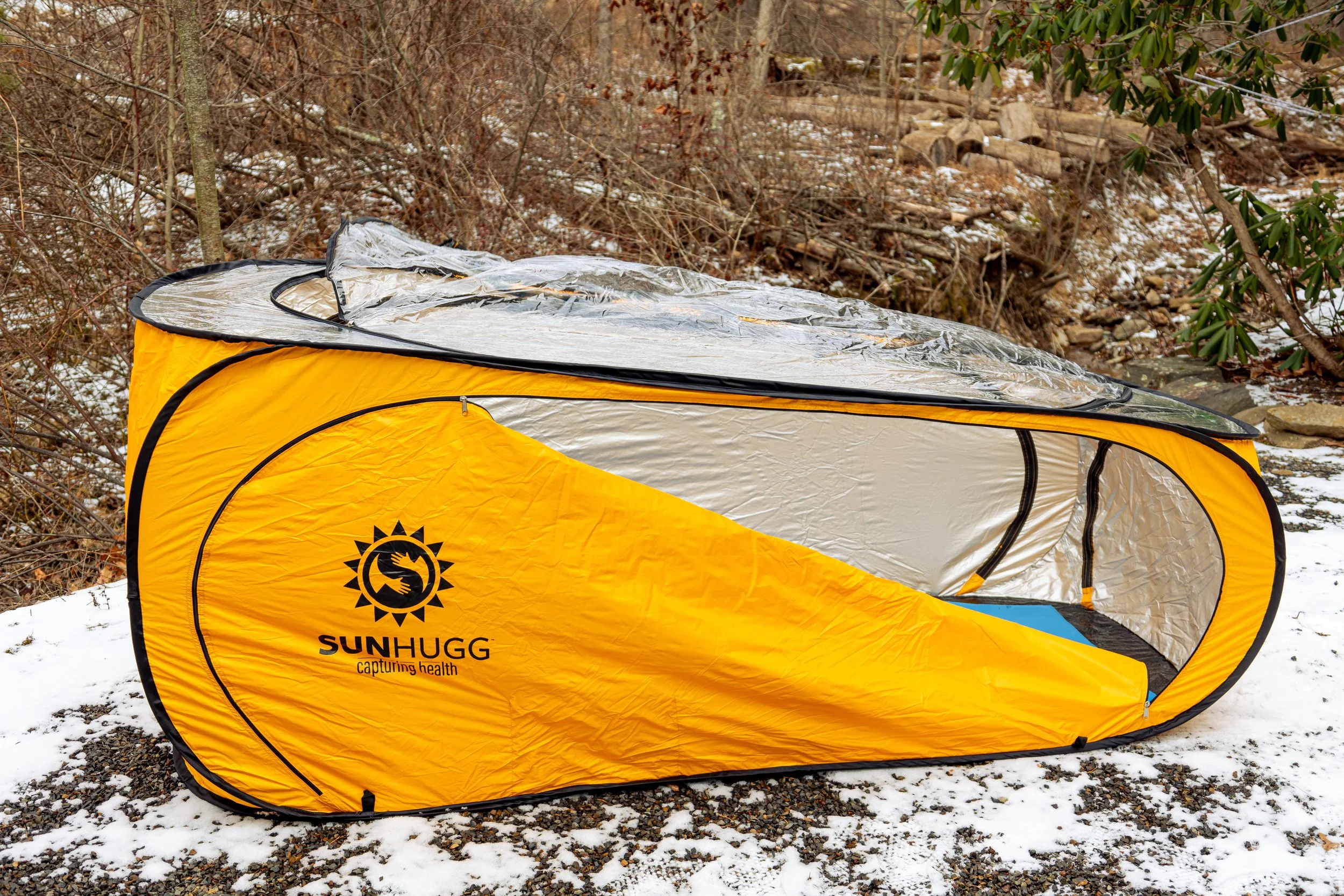 Lifestyle product photography featuring the SunHugg pop-up outdoor shelter, captured in a natural winter setting. Images highlight real-world use, setup and breakdown, interior details, branding elements, and scale to demonstrate functionality, porta