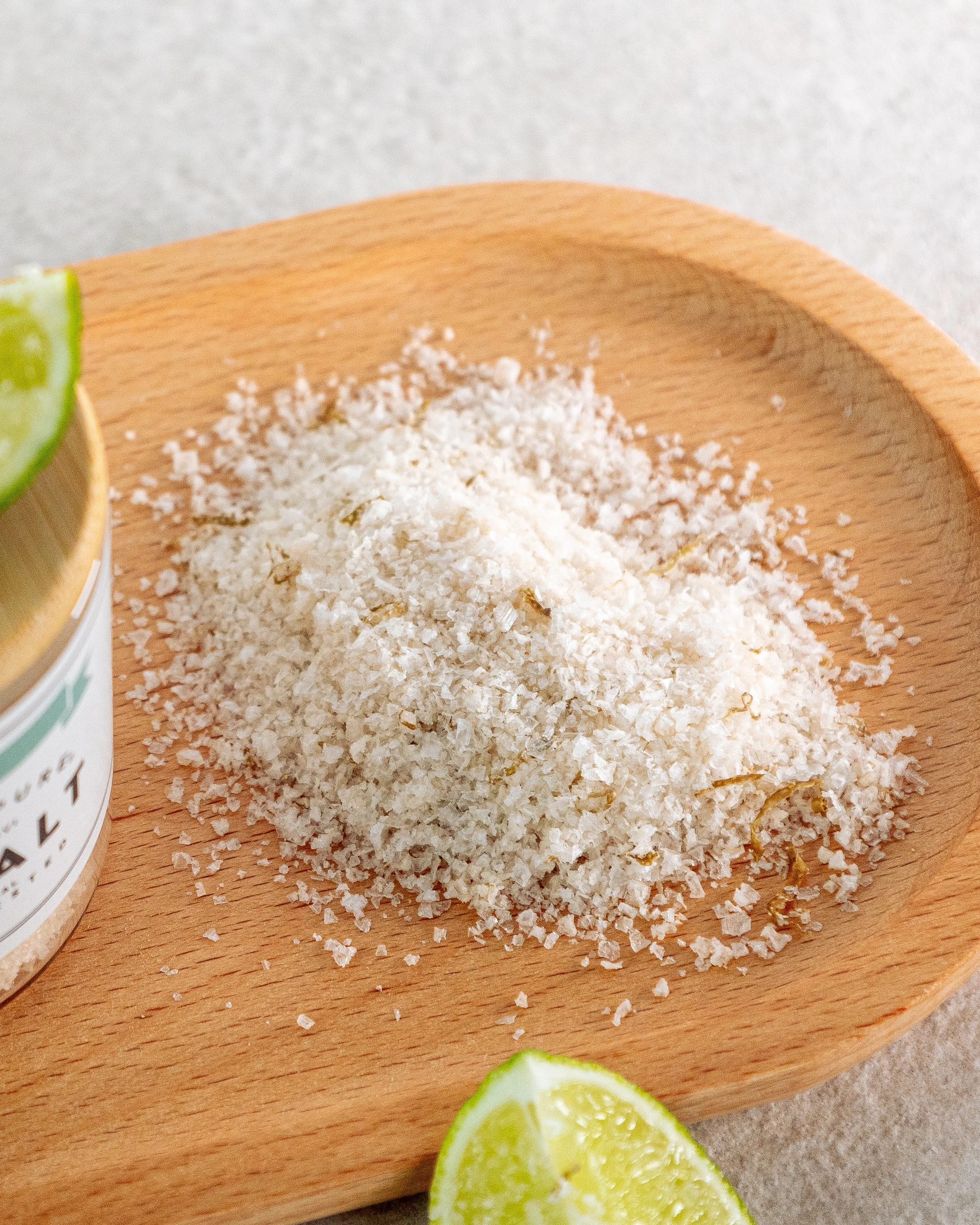 Lime wedges next to a pile of flaky sea salt on a wooden plate.