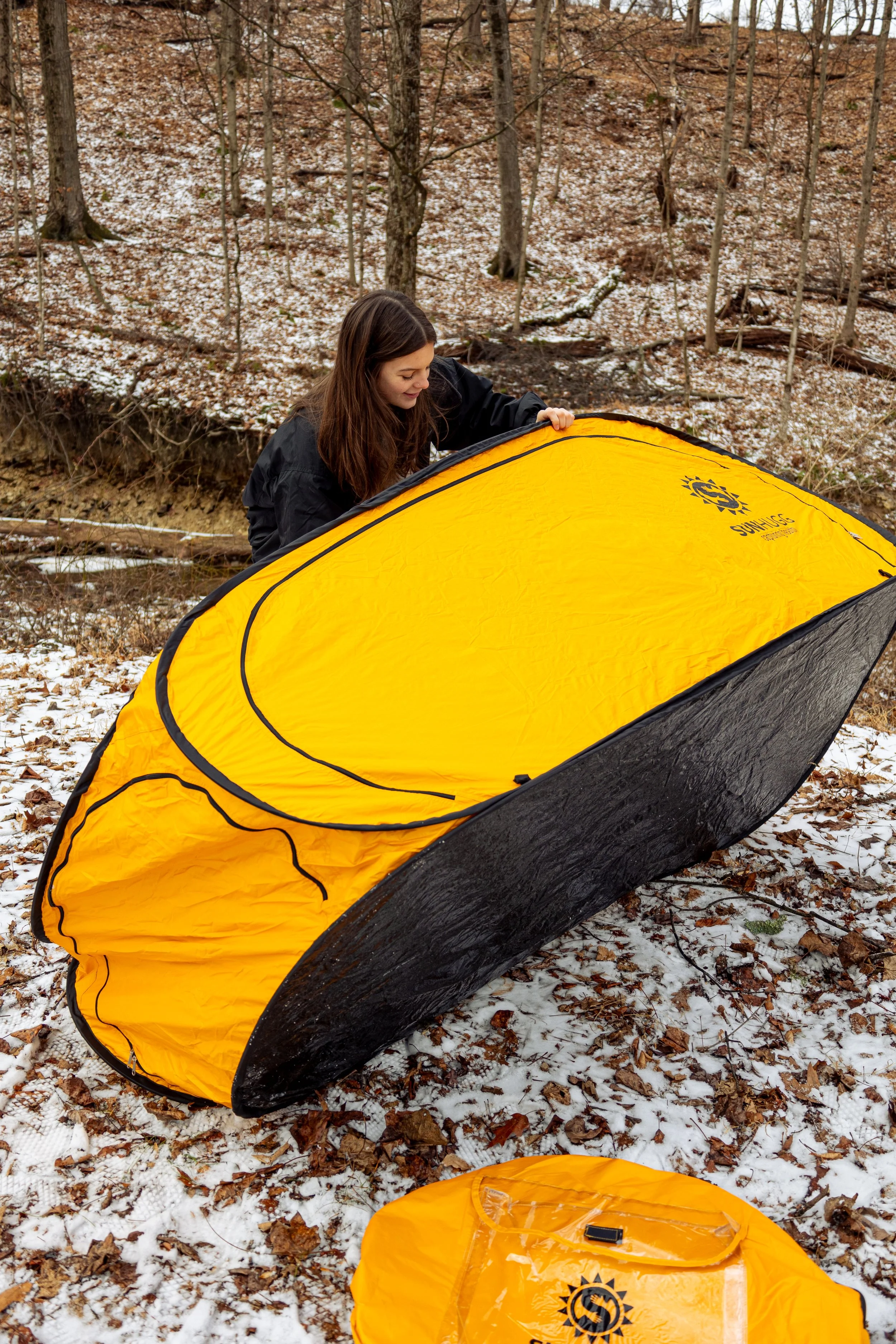 Lifestyle product photography featuring the SunHugg pop-up outdoor shelter, captured in a natural winter setting. Images highlight real-world use, setup and breakdown, interior details, branding elements, and scale to demonstrate functionality, porta