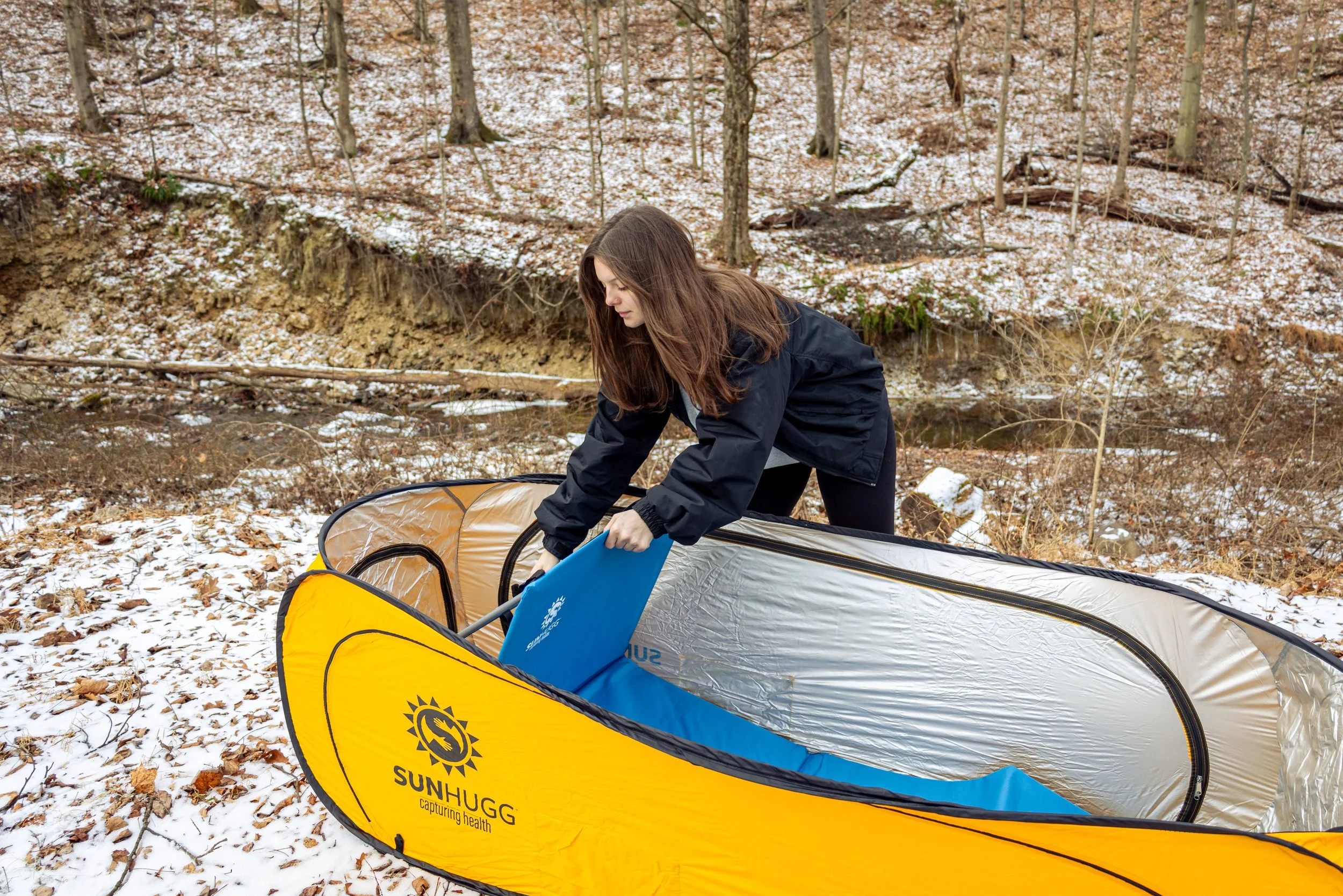Lifestyle product photography featuring the SunHugg pop-up outdoor shelter, captured in a natural winter setting. Images highlight real-world use, setup and breakdown, interior details, branding elements, and scale to demonstrate functionality, porta