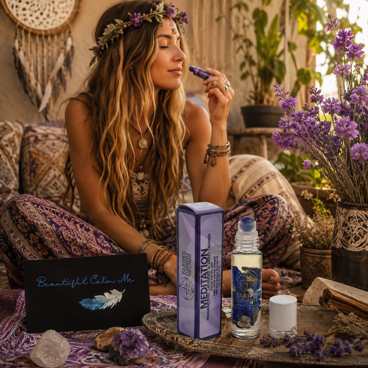 A young woman with long wavy hair wearing a flower crown and bohemian clothing is sitting cross-legged on a bohemian rug. She is using a small essential oil roller on her nose, surrounded by purple flowers, crystals, and wellness products. There is a sign that reads 'Beautiful Calm Me' with a feather illustration, and a box labeled 'Meditation' along with a bottle labeled 'Earth's Elements' on a tray in front of her.