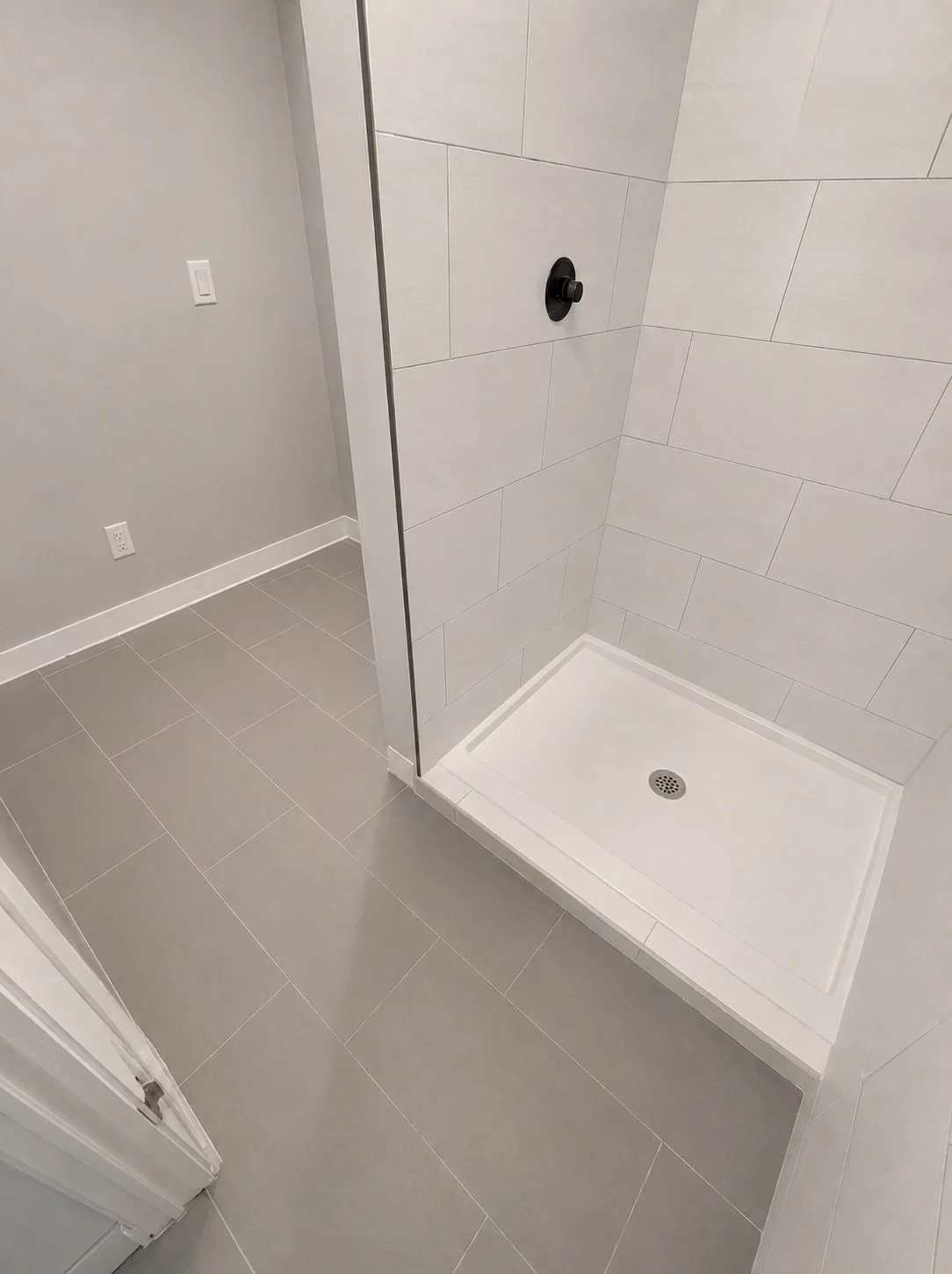 Contemporary bathroom featuring professionally installed gray porcelain floor tile, large-format white porcelain shower wall tile, a walk-in shower with a white shower base, and matte black fixtures for a clean, modern finish.