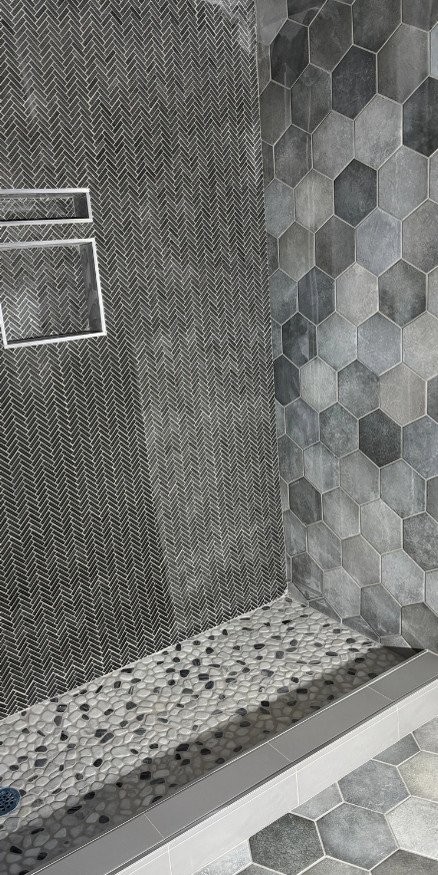 Custom walk-in shower featuring gray hexagon wall tile, herringbone accent tile, and pebble mosaic shower flooring installed by JK Flooring & Tile.