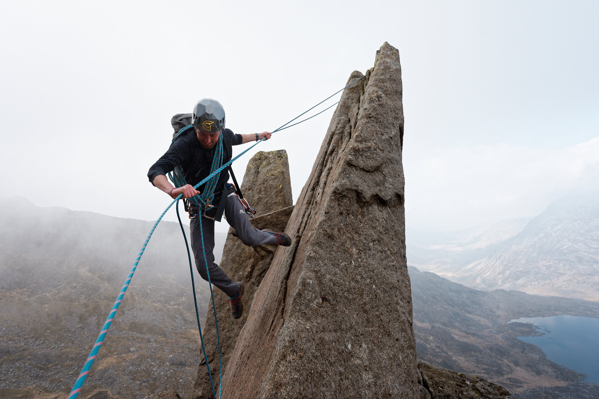 A mountaineer jumping off a spike of rock above the Ogwen valley, Eryri, Wales.