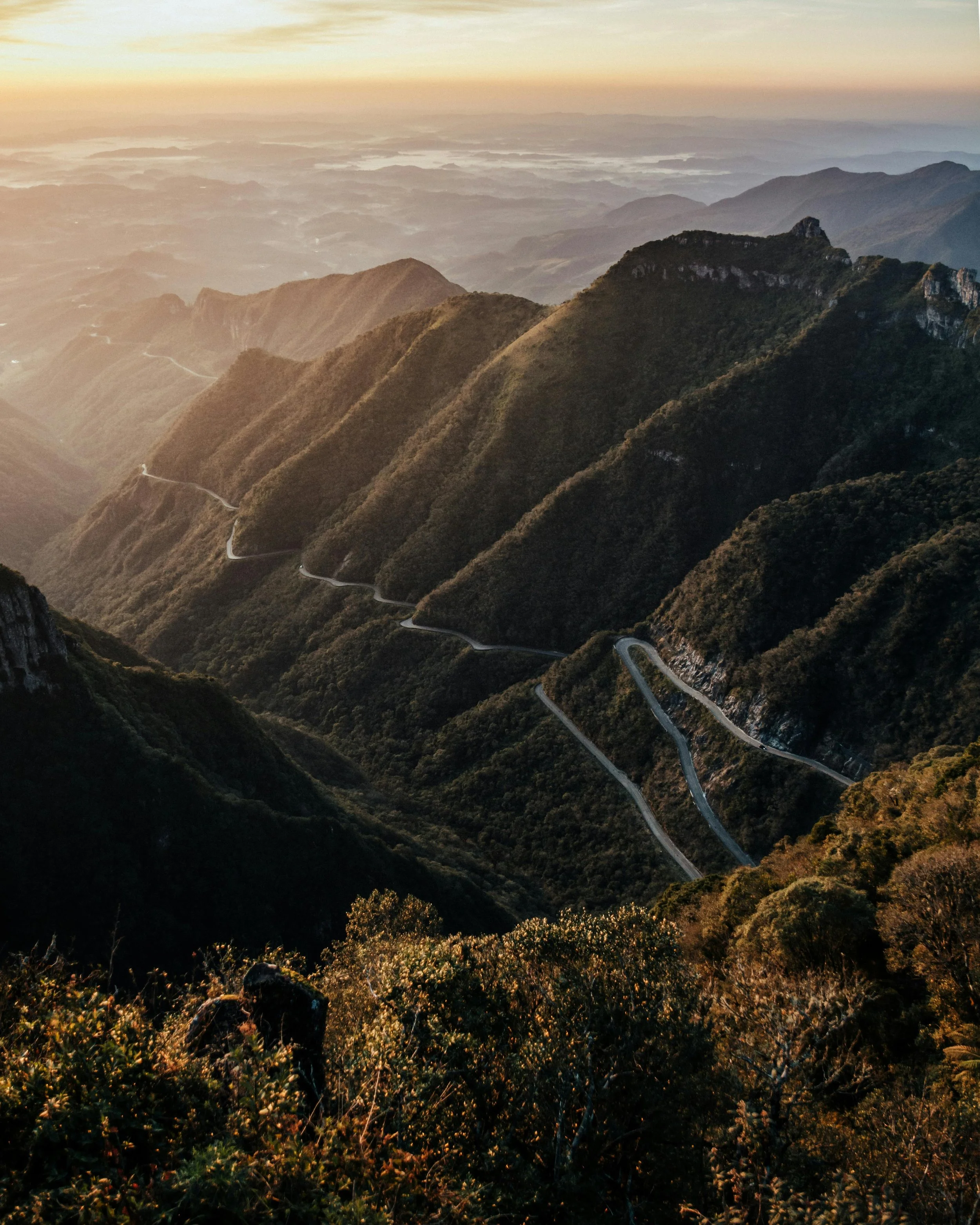 Winding mountain road through lush green mountains at sunrise or sunset.